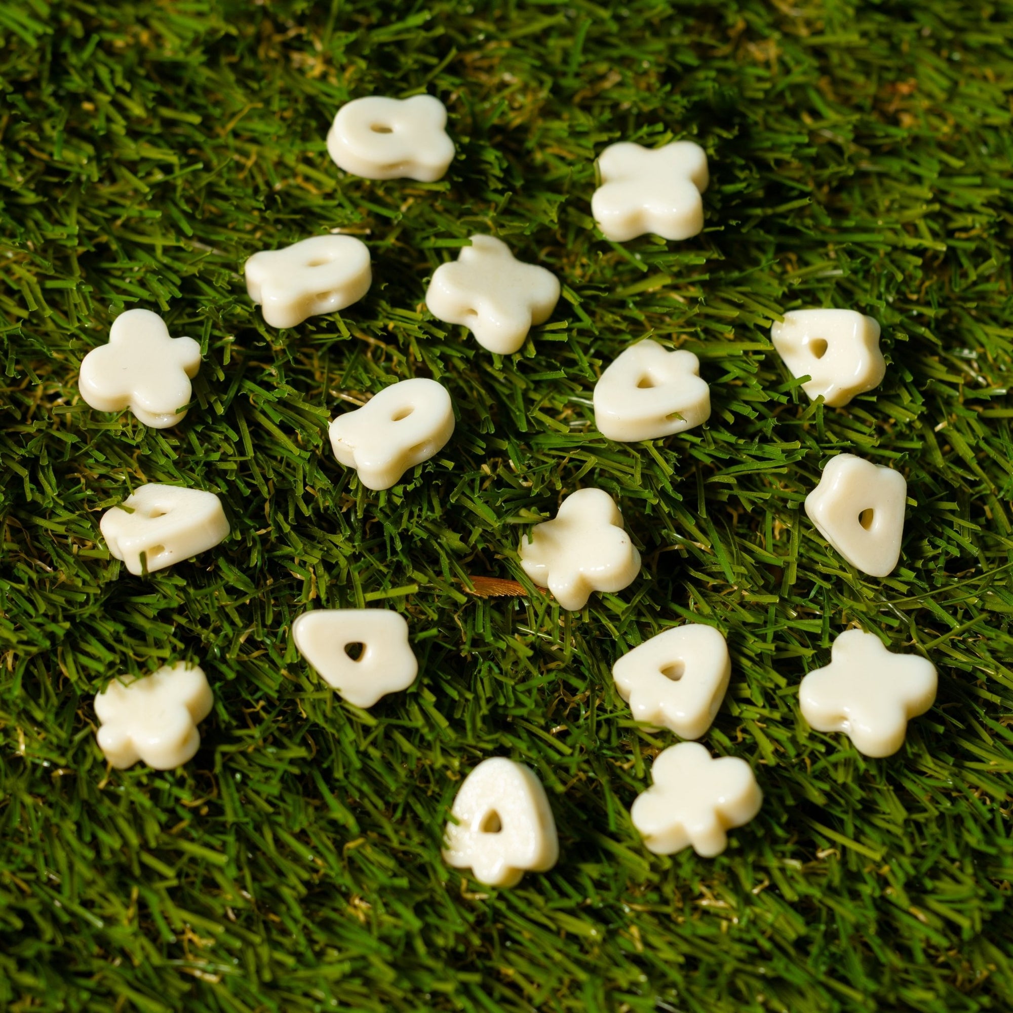 Cream four-leaf clover kandi beads scattered on artificial grass, drilled holes facing up
