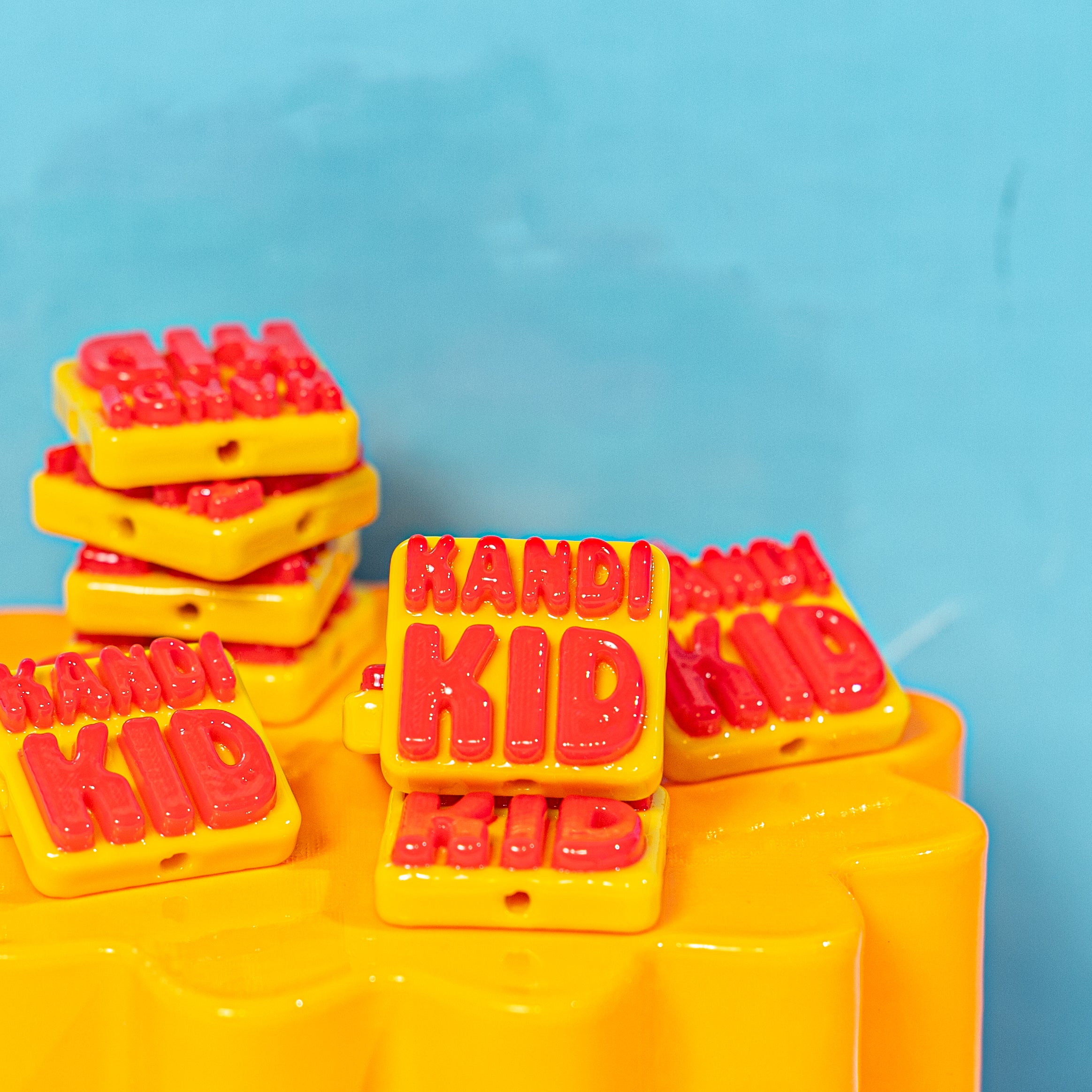 Yellow KANDI KID kandi beads with puffy red letters stacked on a yellow riser