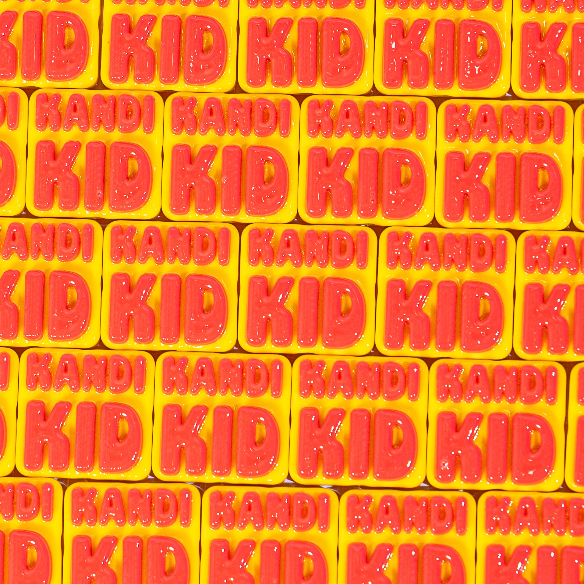 Close-up rows of yellow KANDI KID kandi beads with glossy red lettering