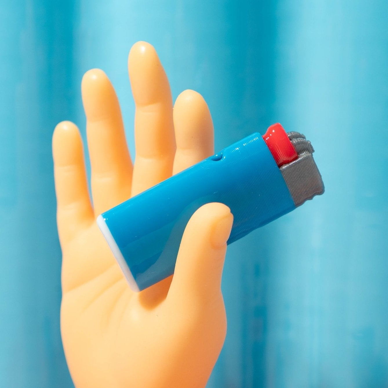 A toy hand holds a blue lighter kandi bead against a streaky blue background