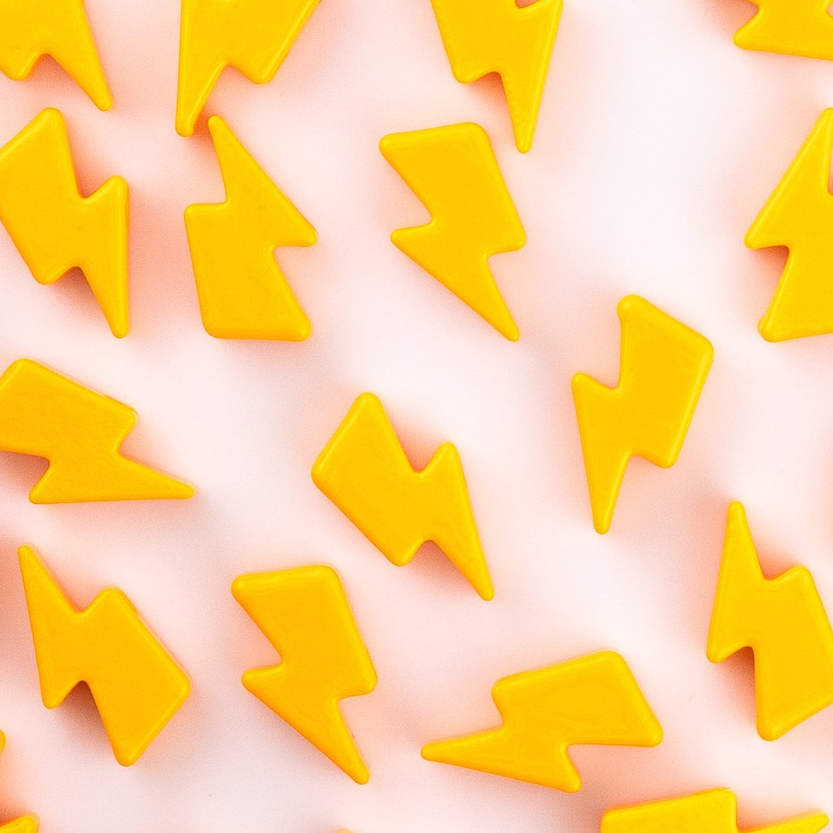 Yellow lightning bolt kandi beads laid out on a soft pink background, from above