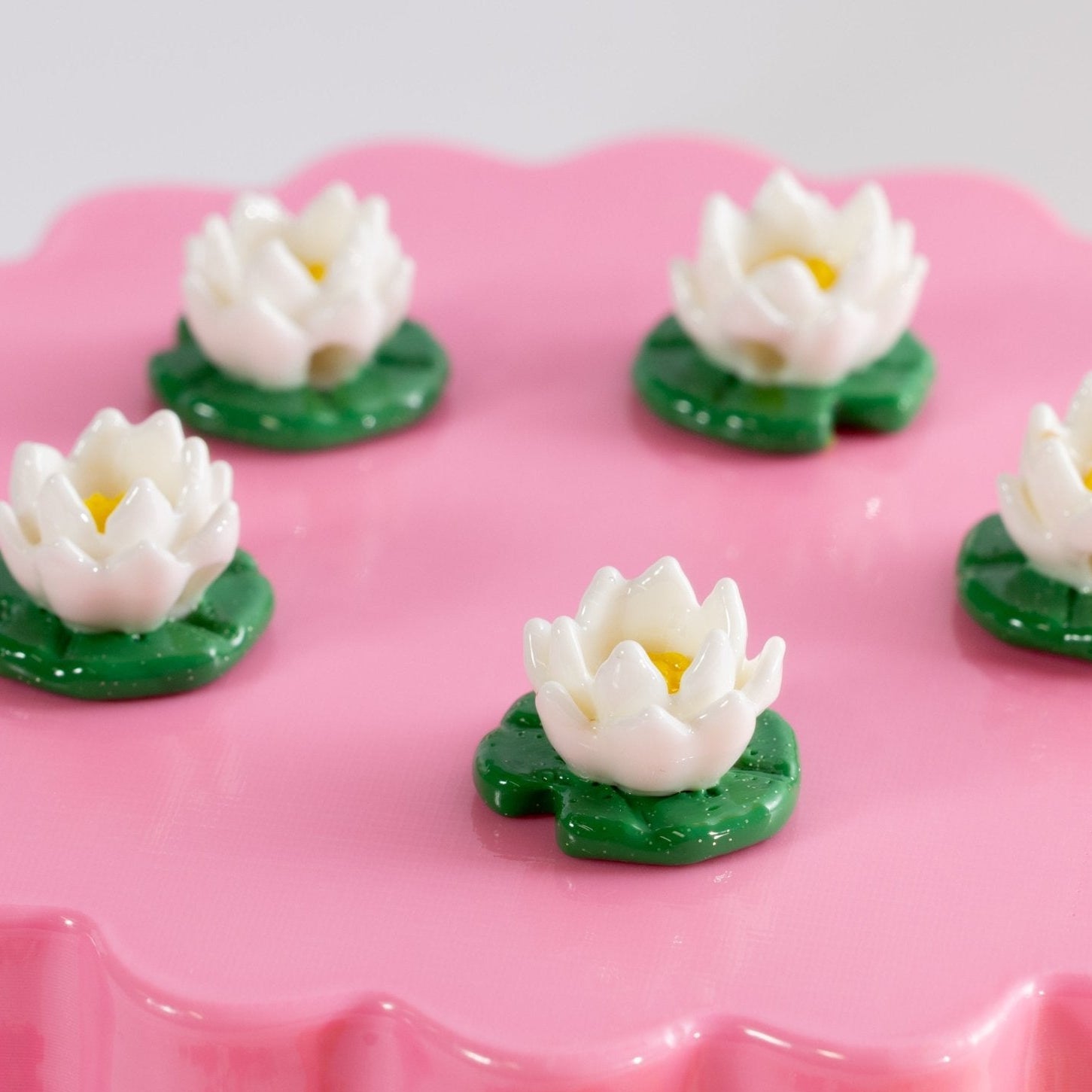 White lotus kandi beads on green lily pads spaced across a pink scalloped riser