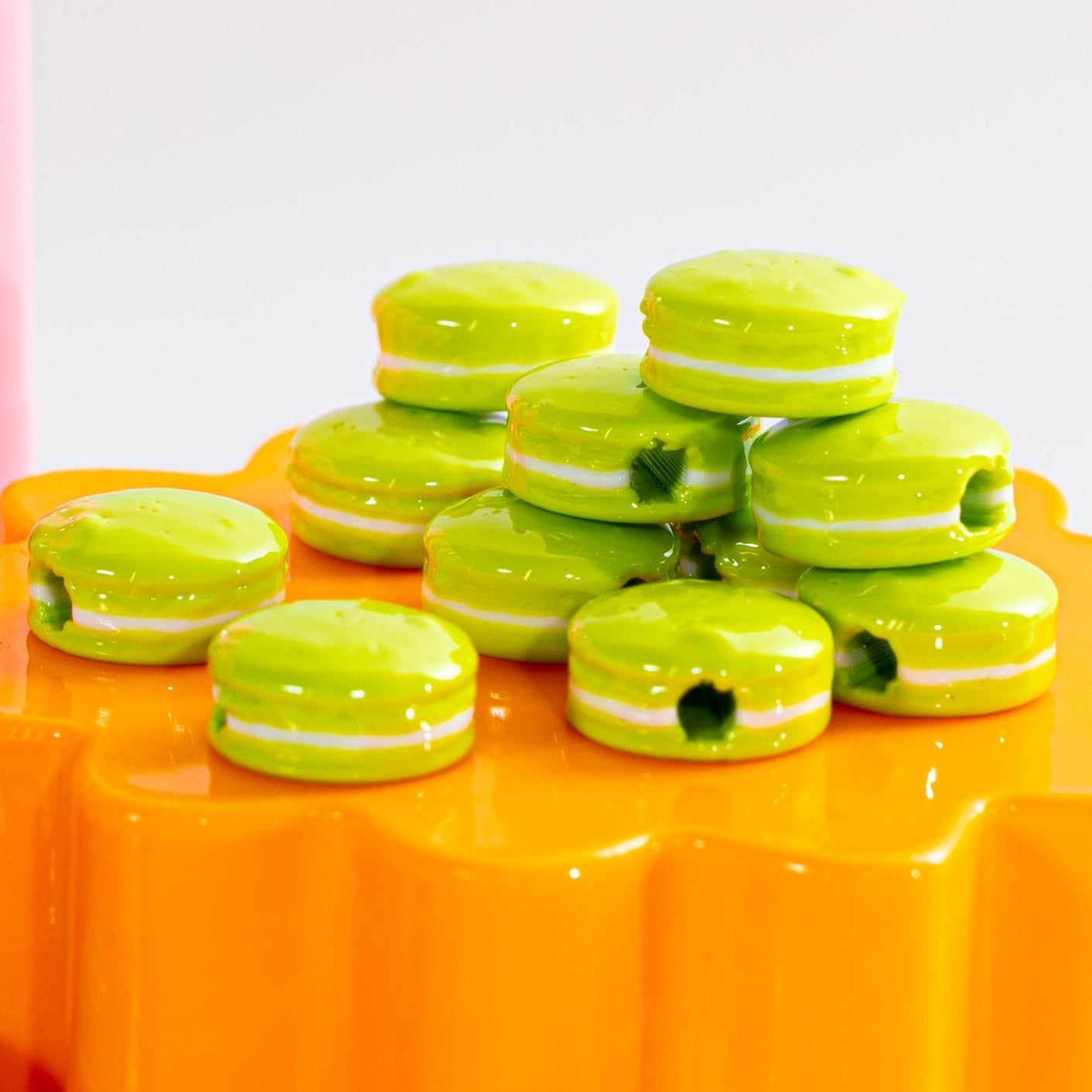 Lime green macaron beads piled and stacked on a glossy orange riser, seen at eye level