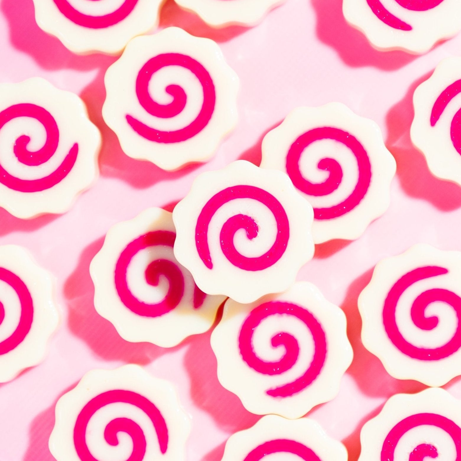 Pink and white swirl fish cake kandi beads scattered on a pink surface, seen from above