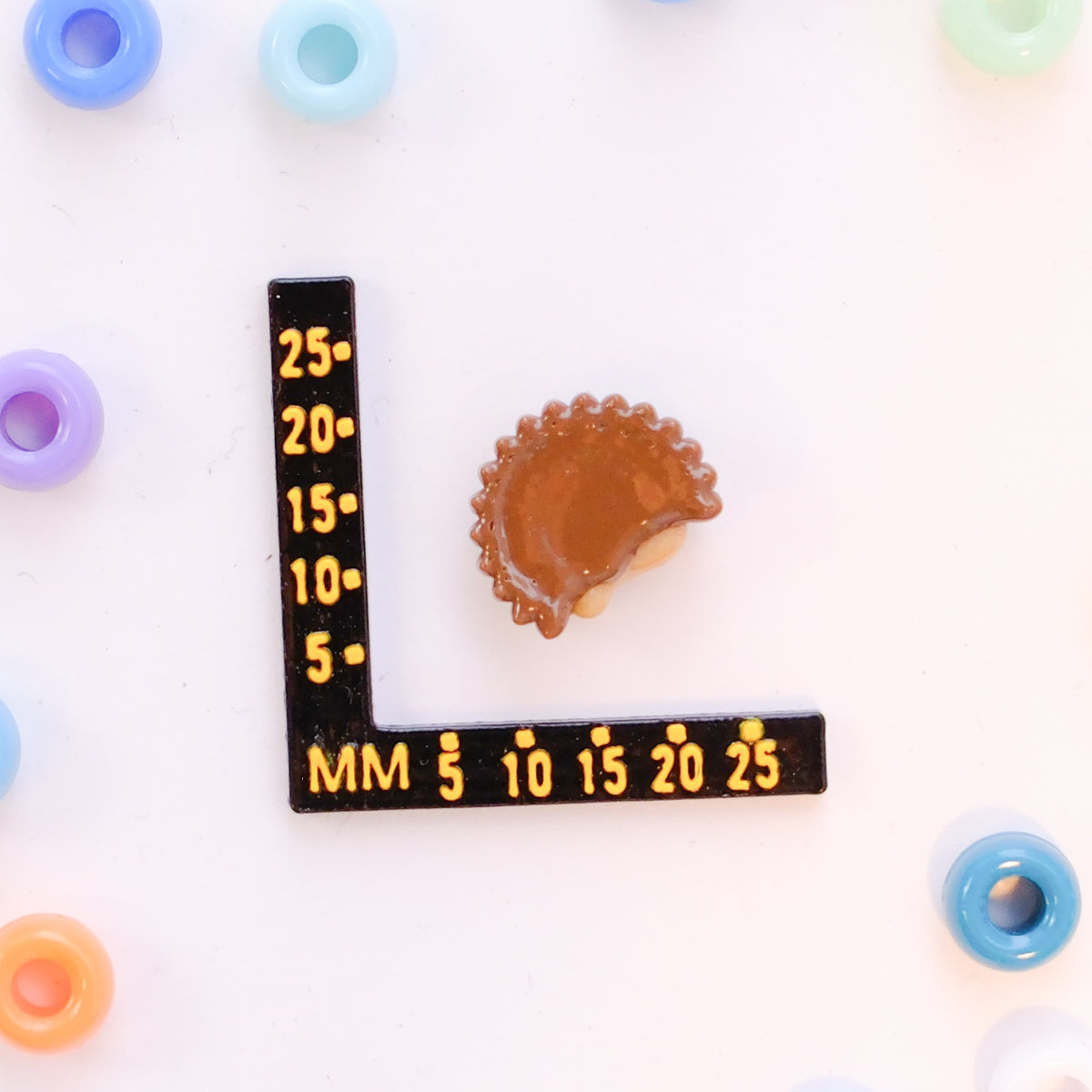 Size guide: a peanut butter cup kandi bead beside a millimeter ruler for scale
