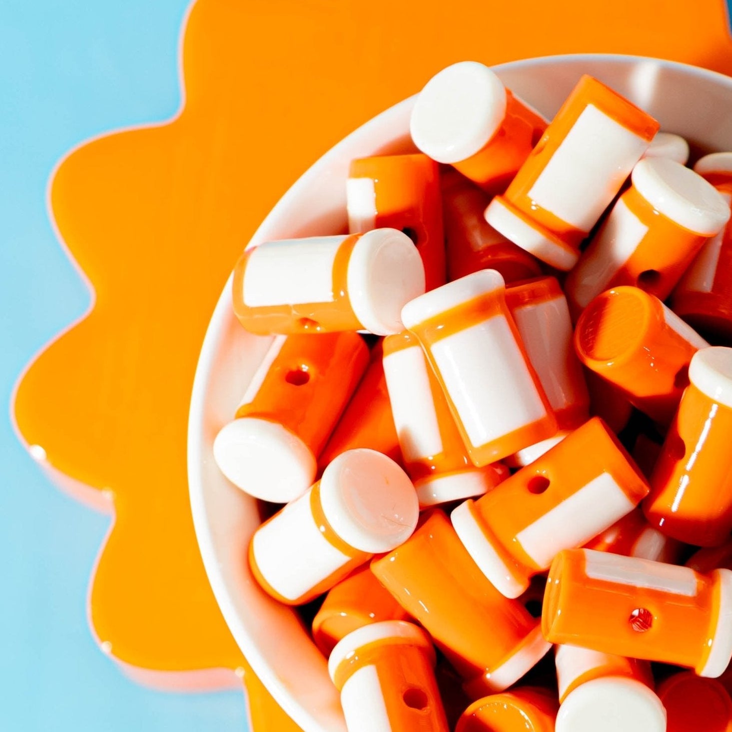 Orange pill bottle kandi beads heaped in a white bowl, orange and blue behind