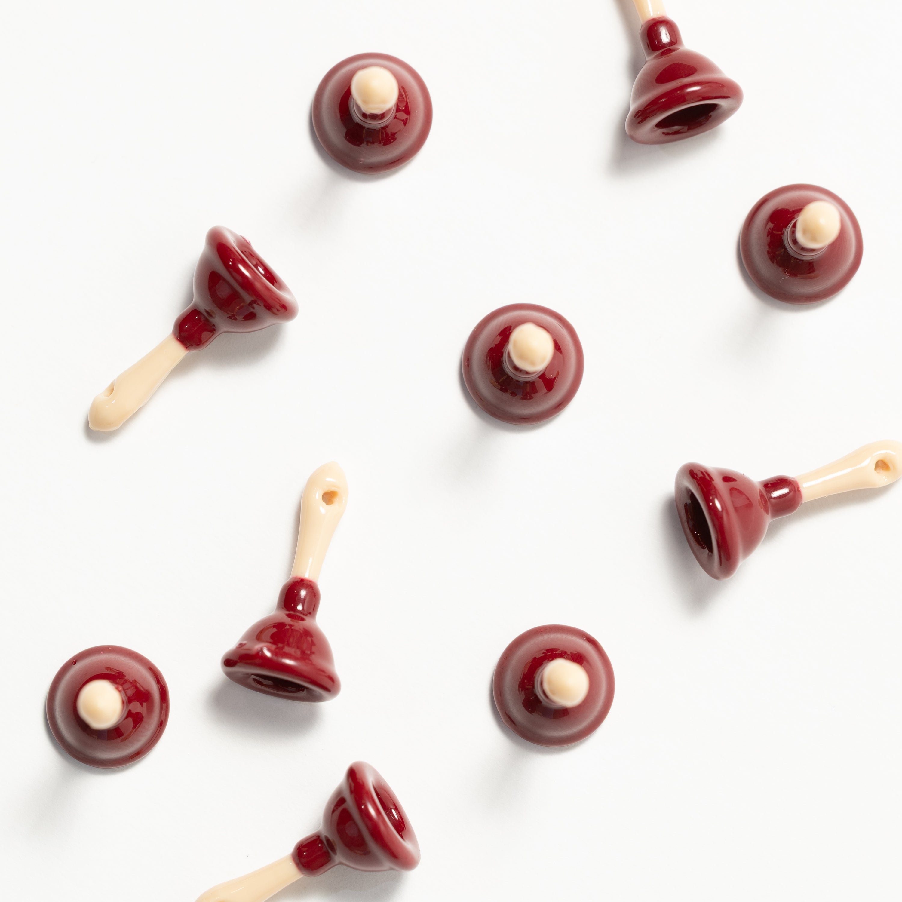 Maroon plunger kandi beads scattered on white, cream handles drilled for stringing