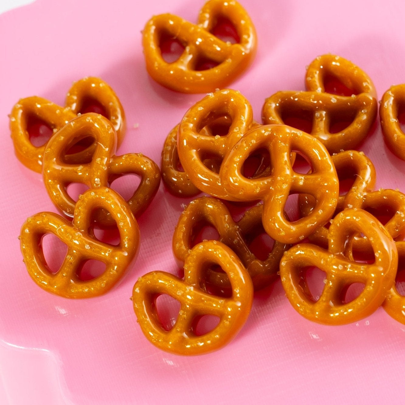 Salted pretzel beads piled together on a glossy pink surface, close up