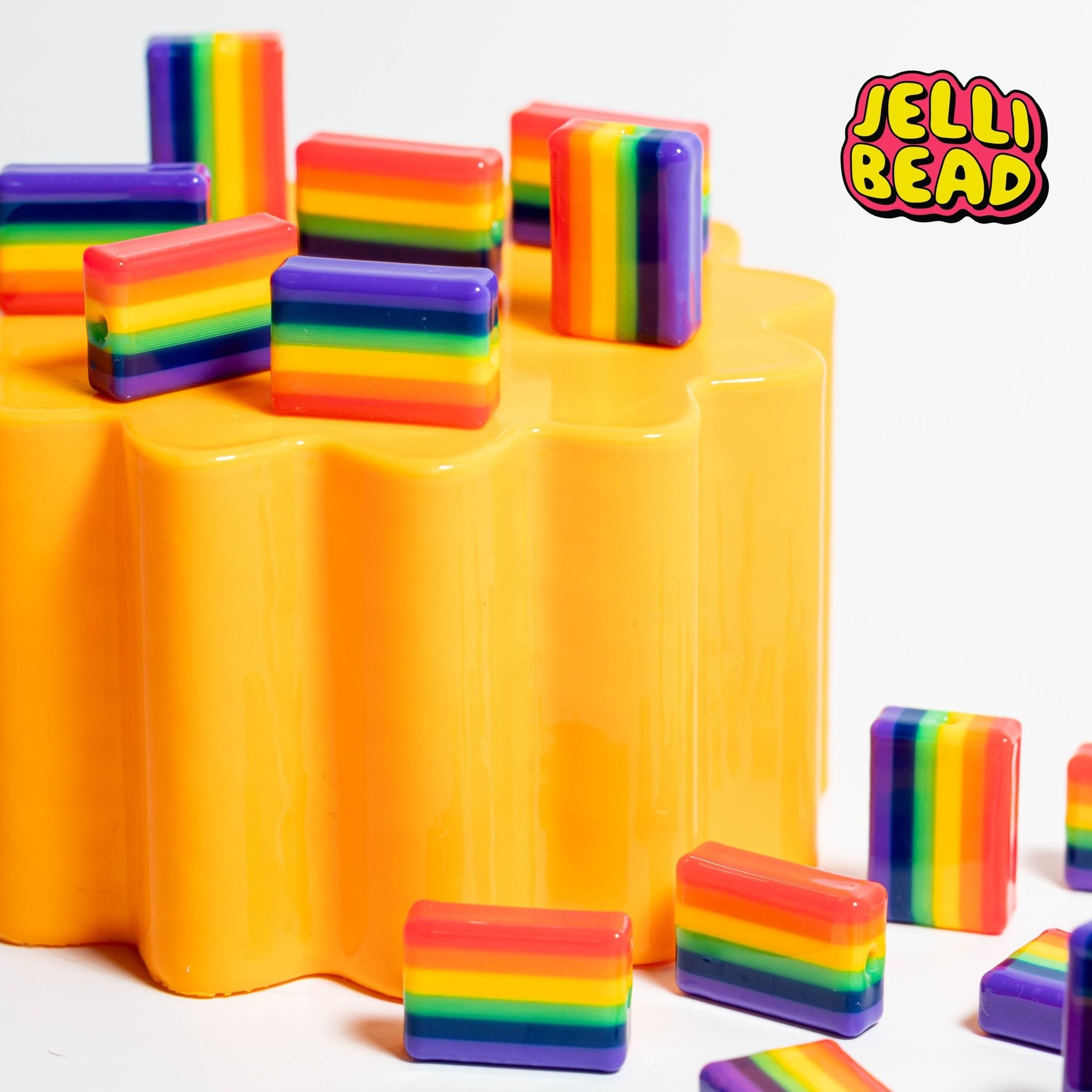 Pride flag kandi beads standing on a yellow wavy riser with more scattered below