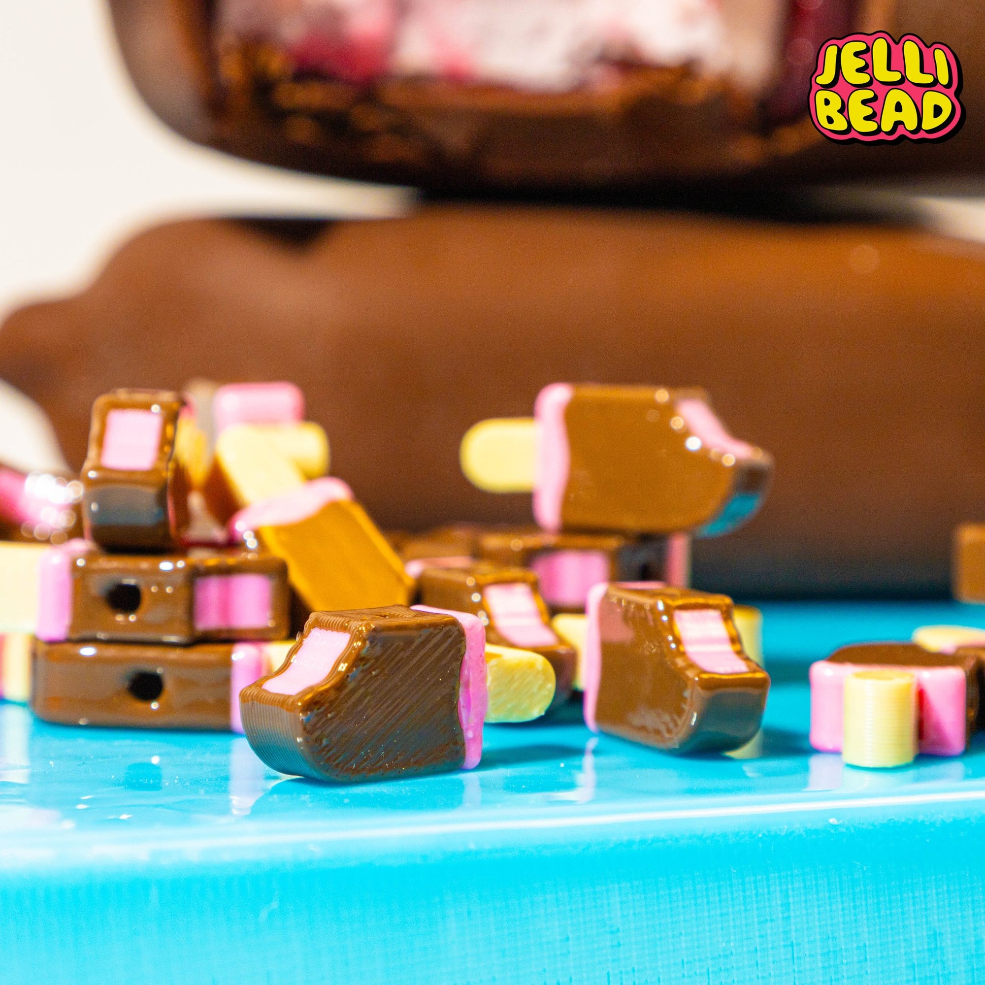 Close-up of raspberry fudgesicle kandi beads piled on blue, a chocolate bar blurred behind