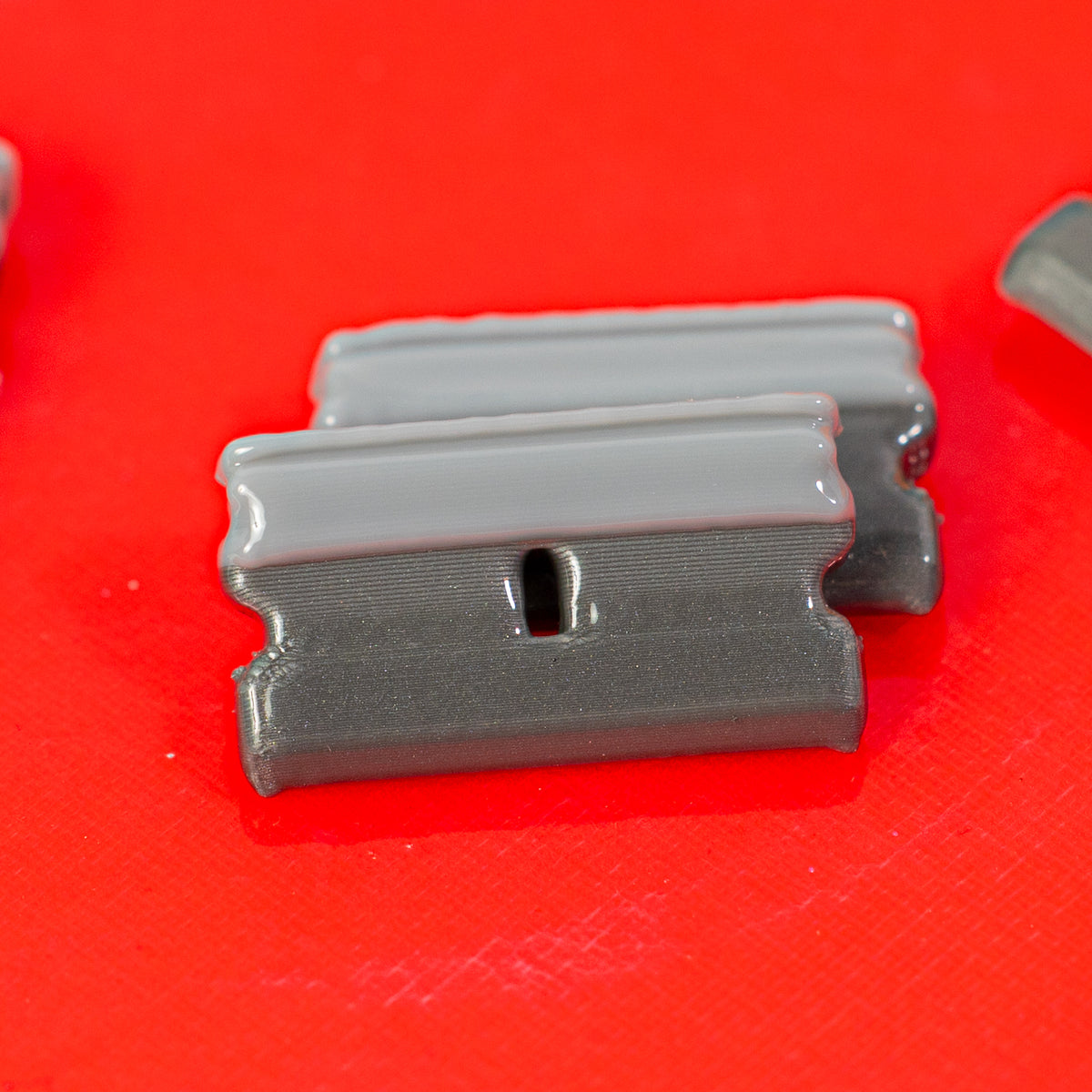 Close-up of gray razor blade kandi beads on a red surface, drilled hole visible