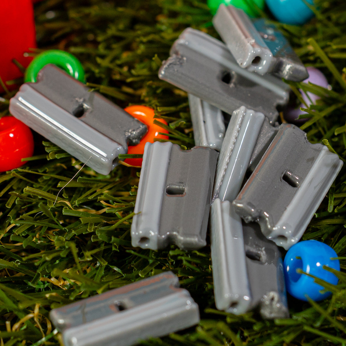 Pile of two-tone gray razor blade kandi beads in green grass