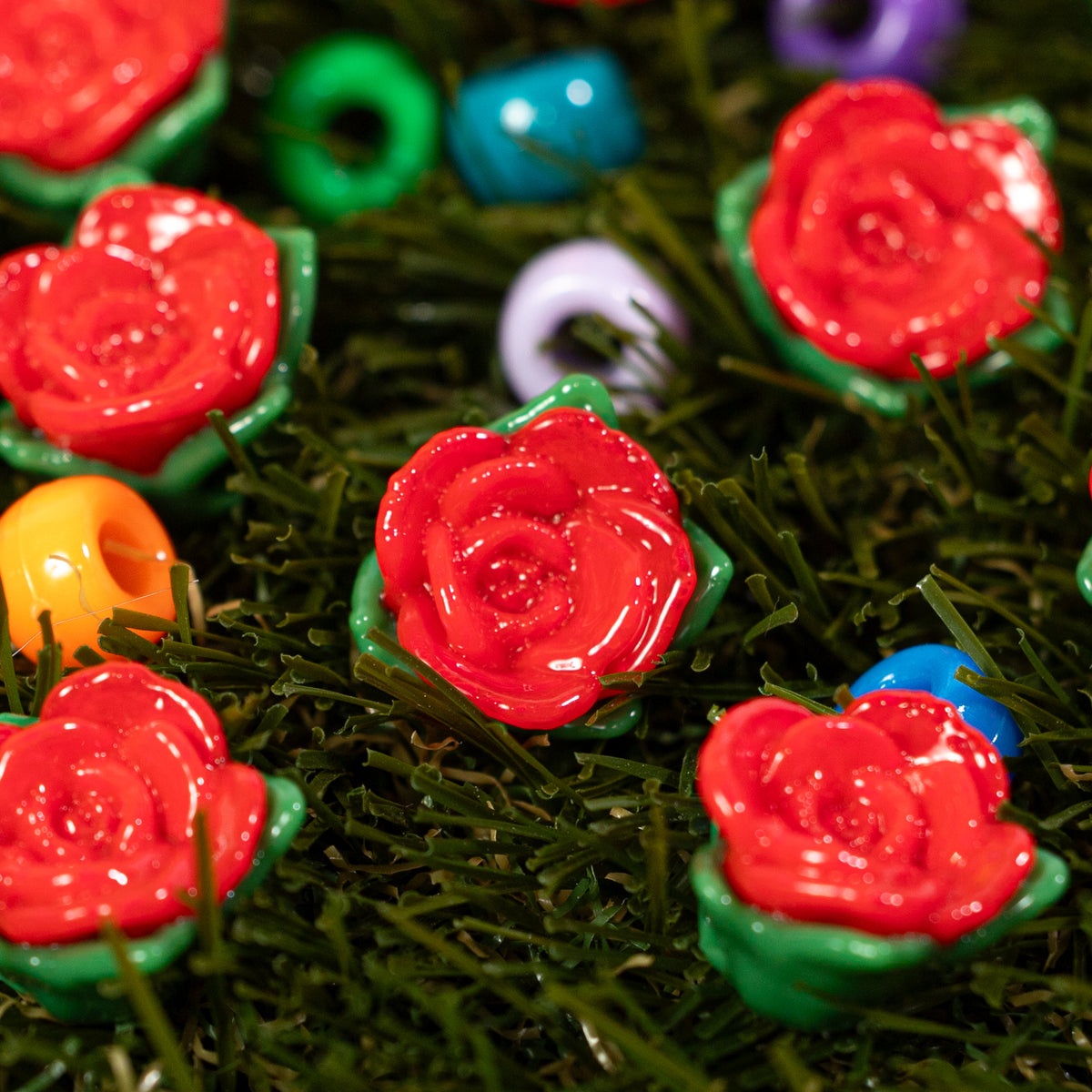 Close-up of red rose kandi beads with green leaves nestled in green grass