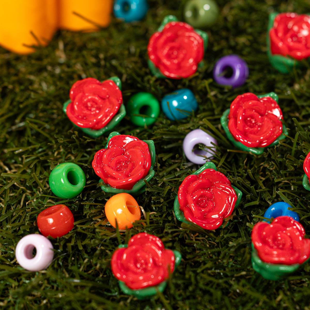 Red and green rose kandi beads scattered on grass among colorful pony beads