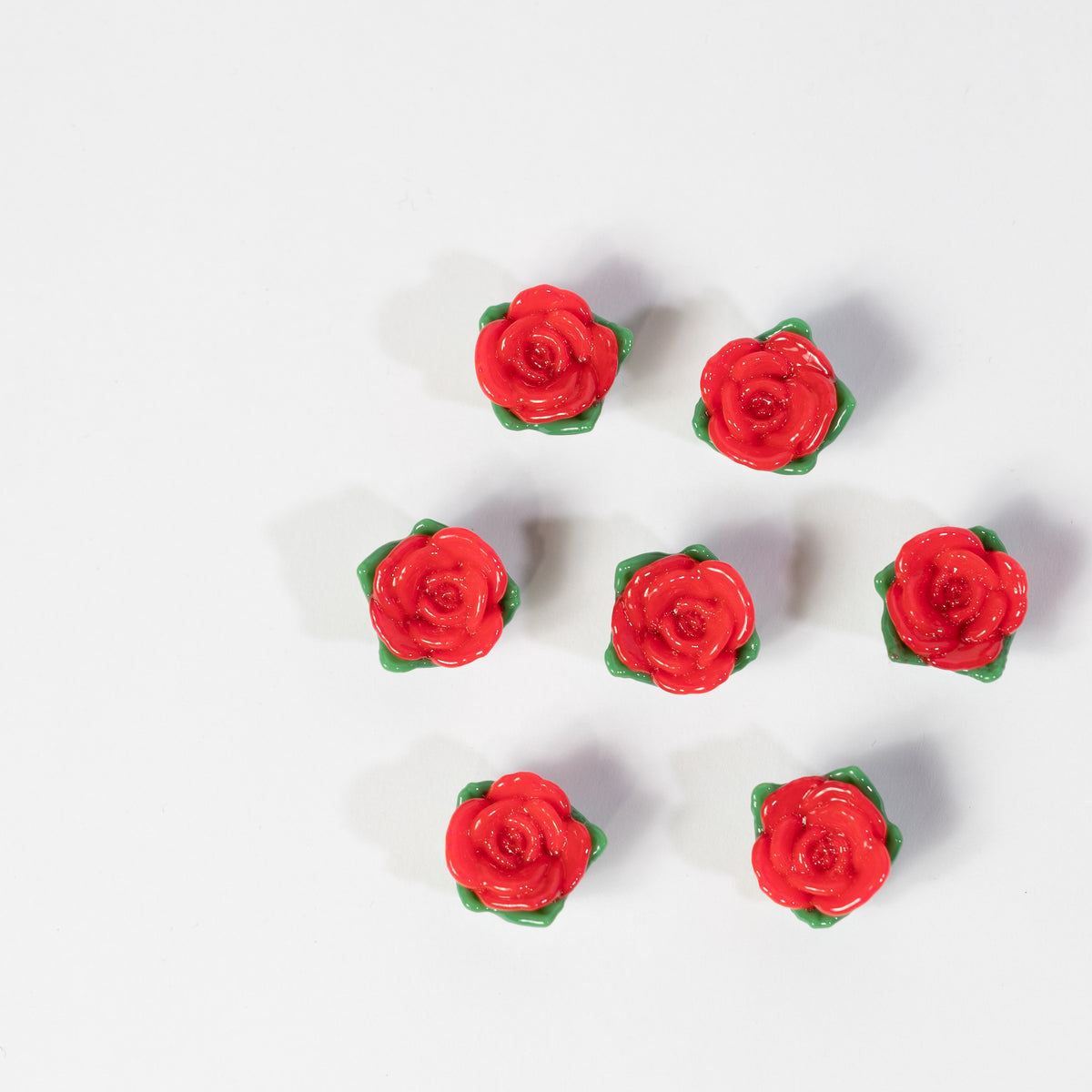 Seven red rose kandi beads with green leaves arranged on white
