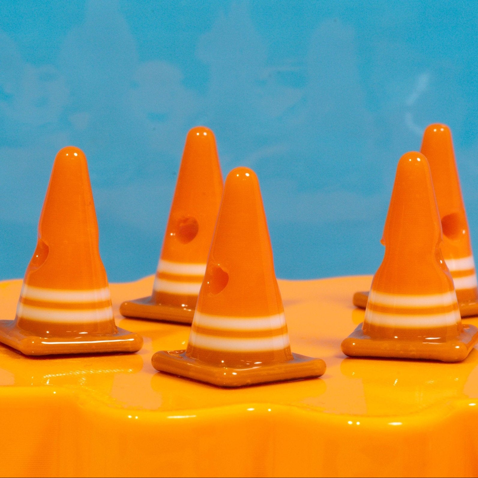 Orange safety cone kandi beads with white stripes standing on a glossy yellow riser against blue