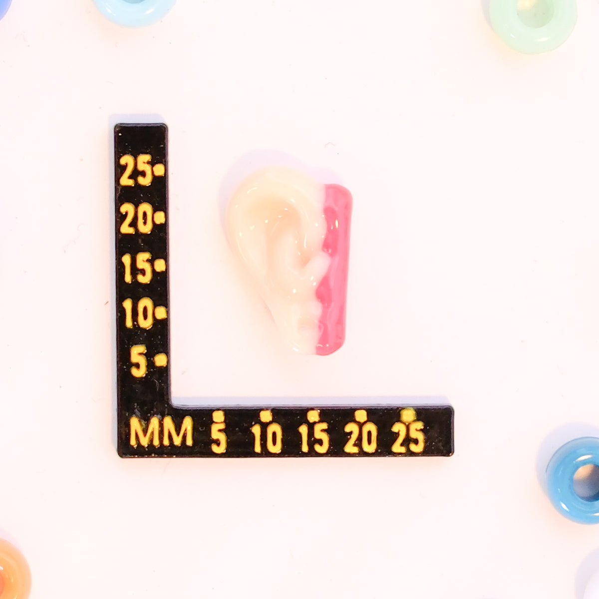 Size guide: a severed ear kandi bead beside a millimeter ruler for scale