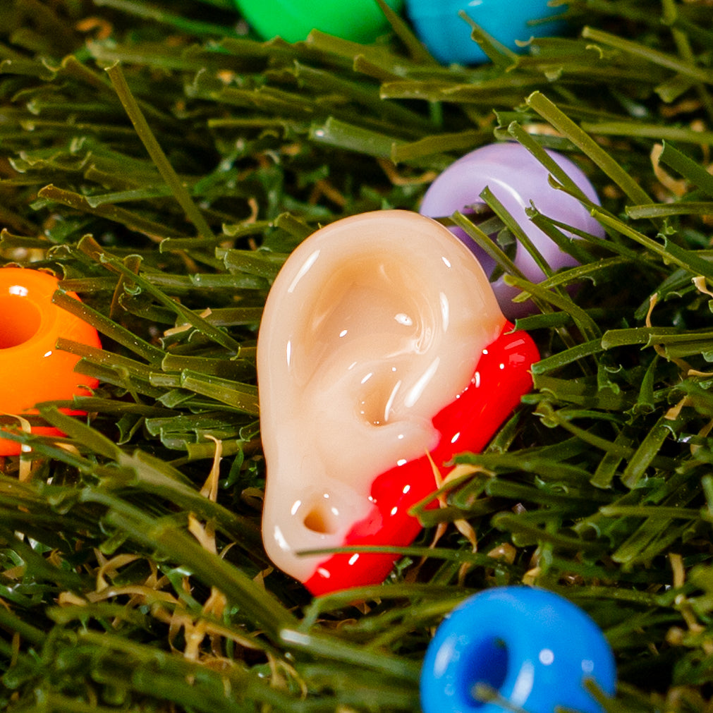 Single severed ear kandi bead in green grass with colorful beads
