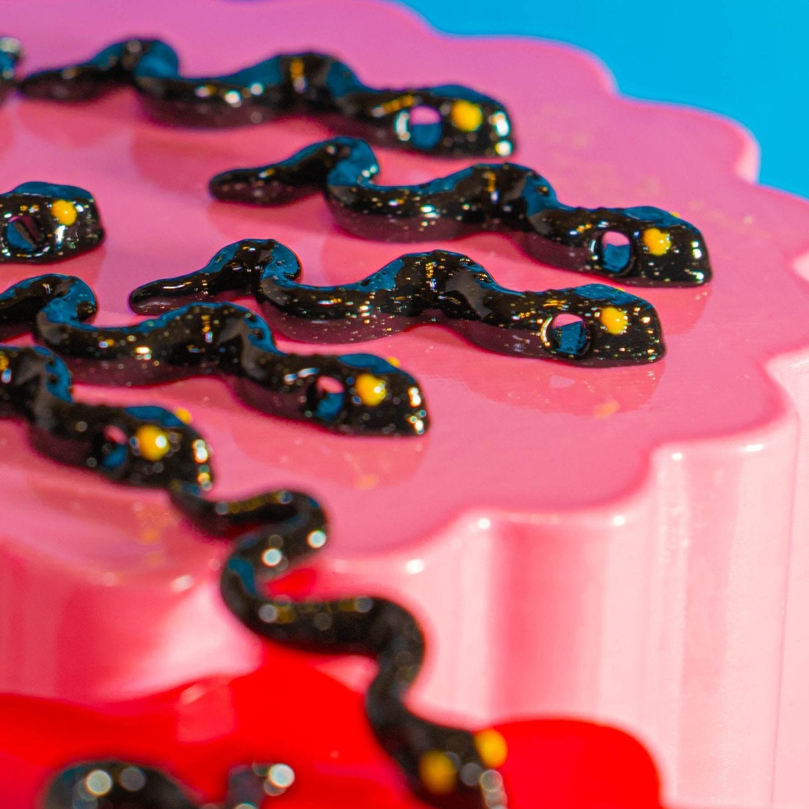 Snake beads for kandi bracelets slithering across a scalloped pink riser, close-up at an angle