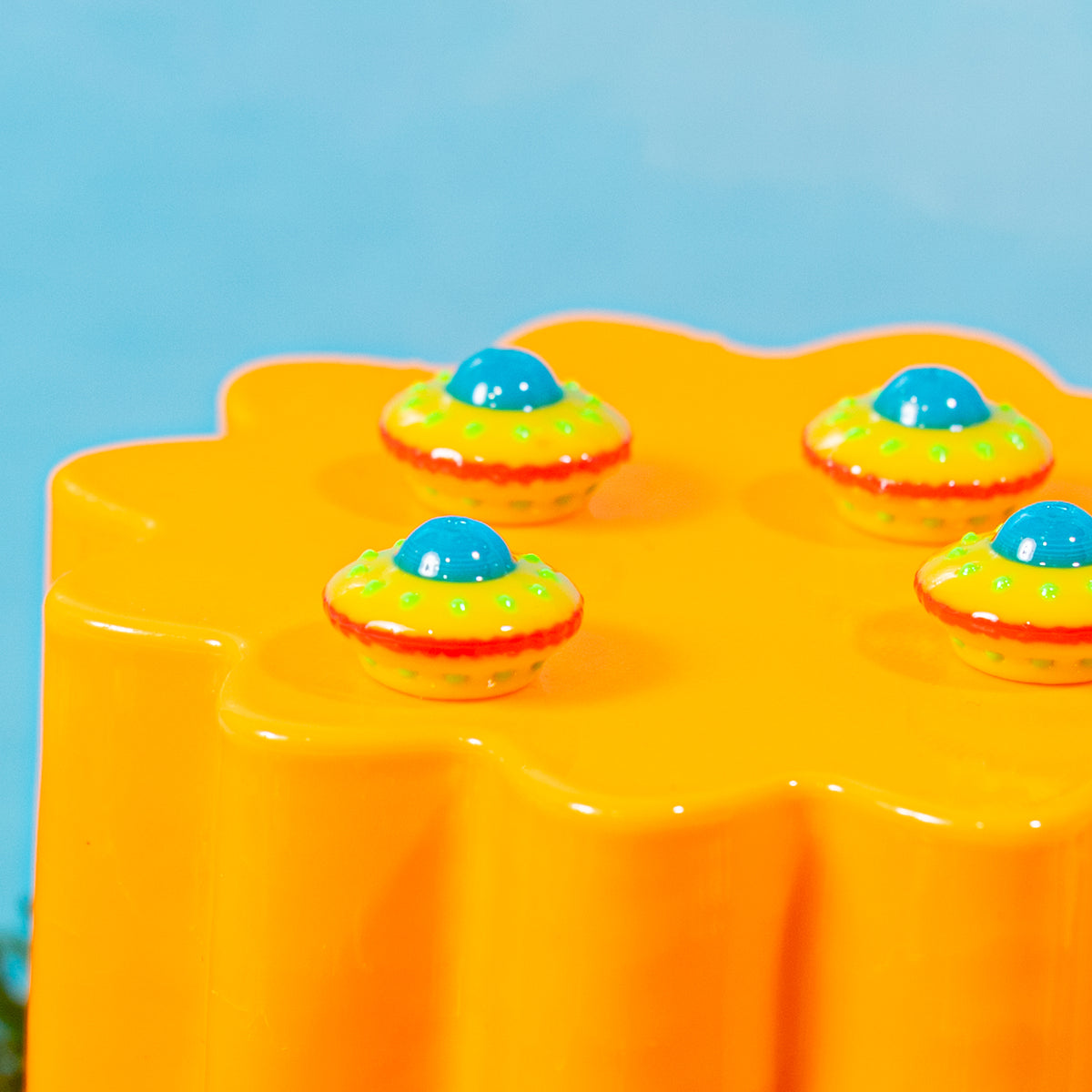 Close-up of four yellow UFO spaceship kandi beads with blue domes and green lights on an orange riser