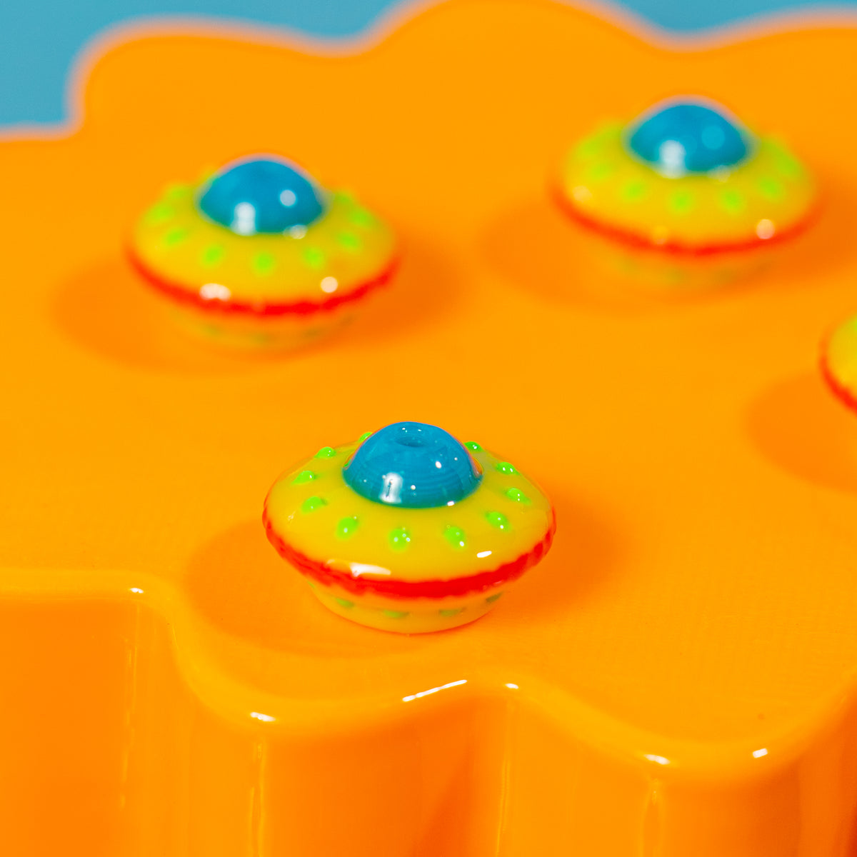 UFO kandi beads with green dotted lights and blue cockpits spaced across an orange block