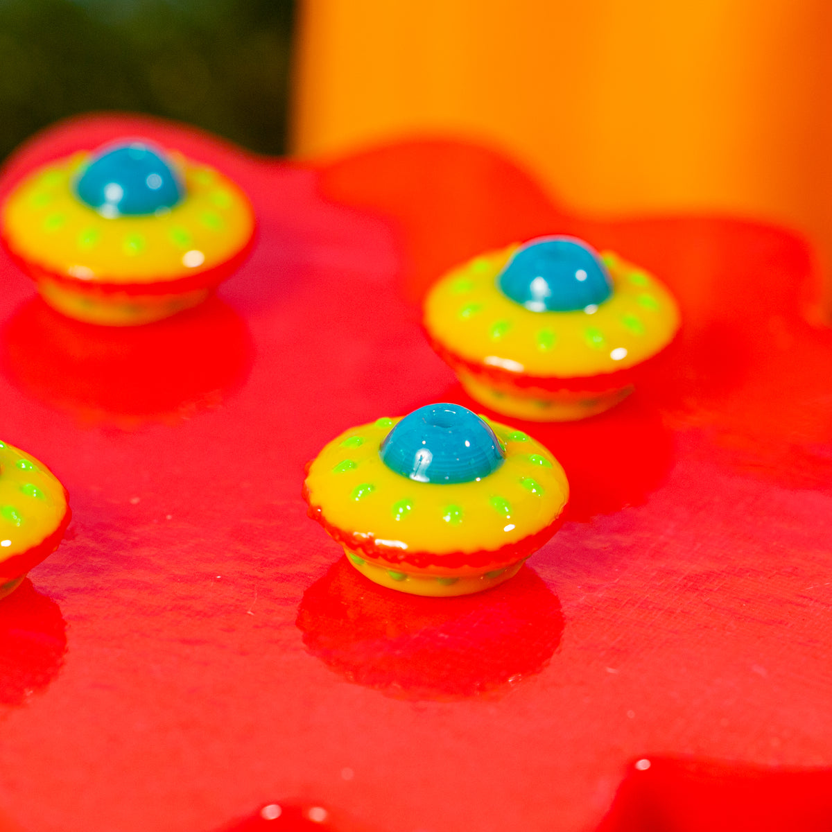 Yellow and red flying saucer kandi beads reflected on a shiny red riser, top holes visible