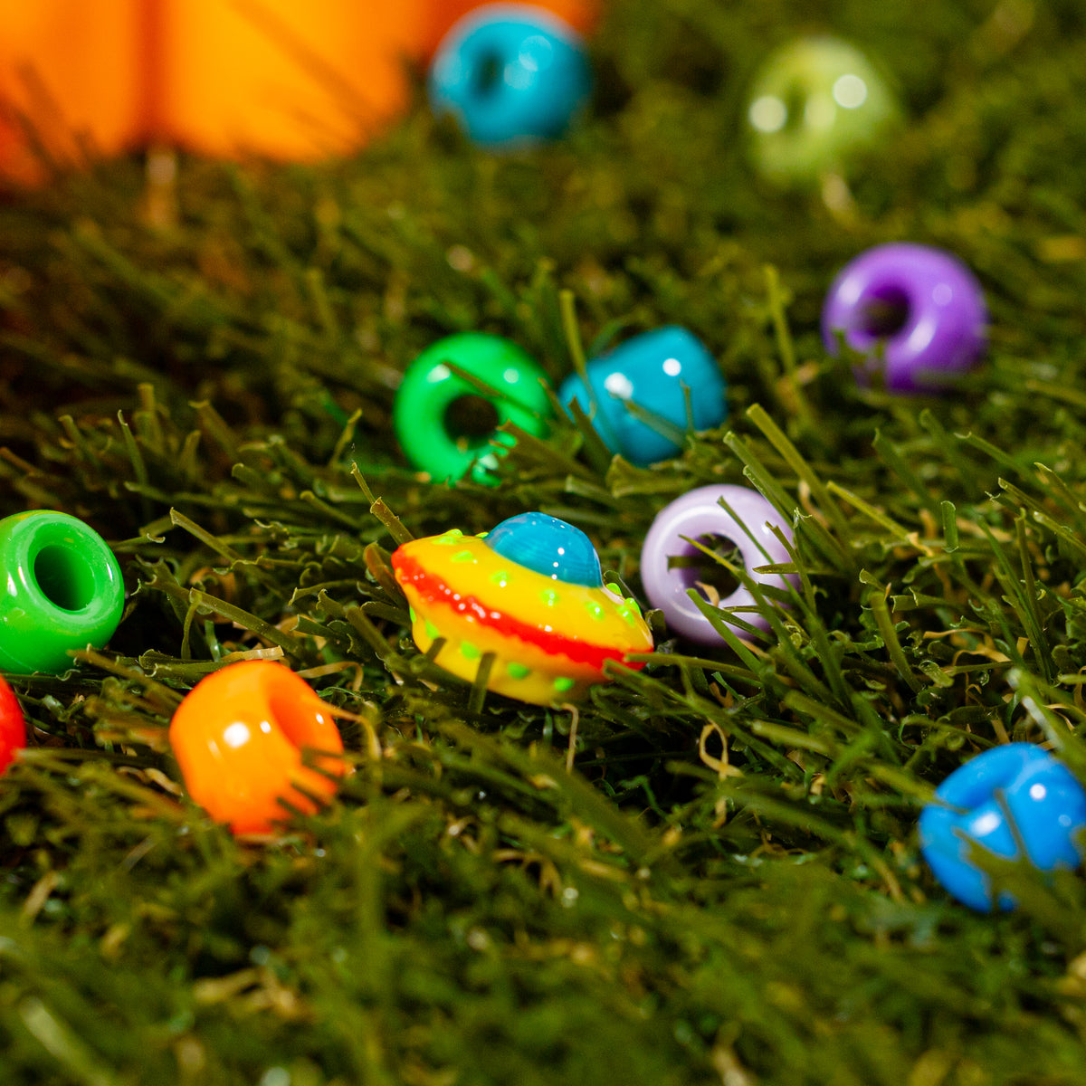 Spaceship kandi bead landed in green grass among colorful kandi beads