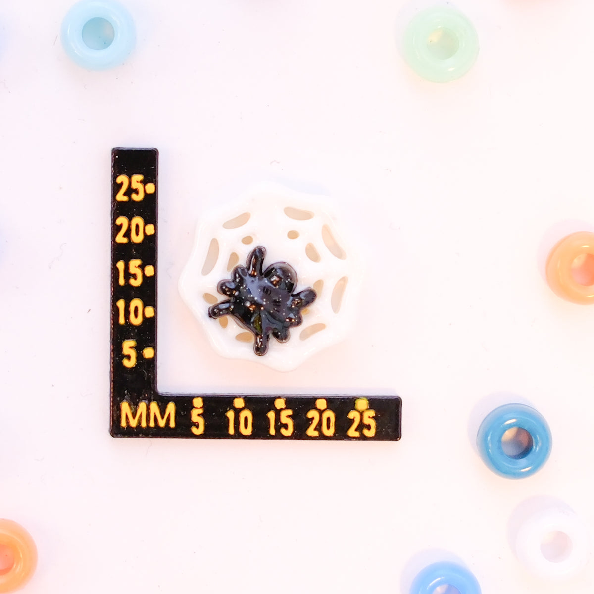 Size guide: a spider web kandi bead beside a millimeter ruler for scale