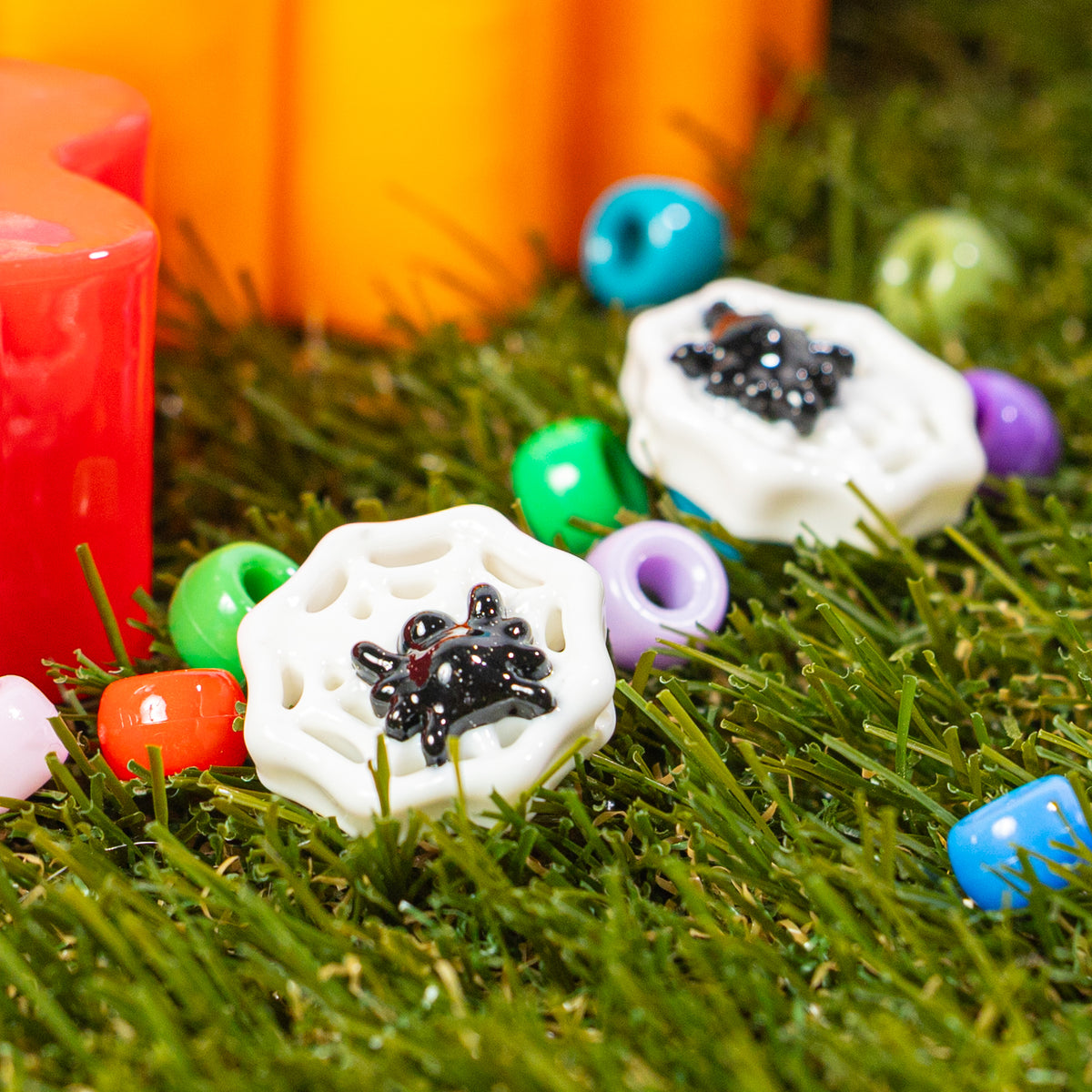 Spider web kandi bead nestled in green grass among colorful beads