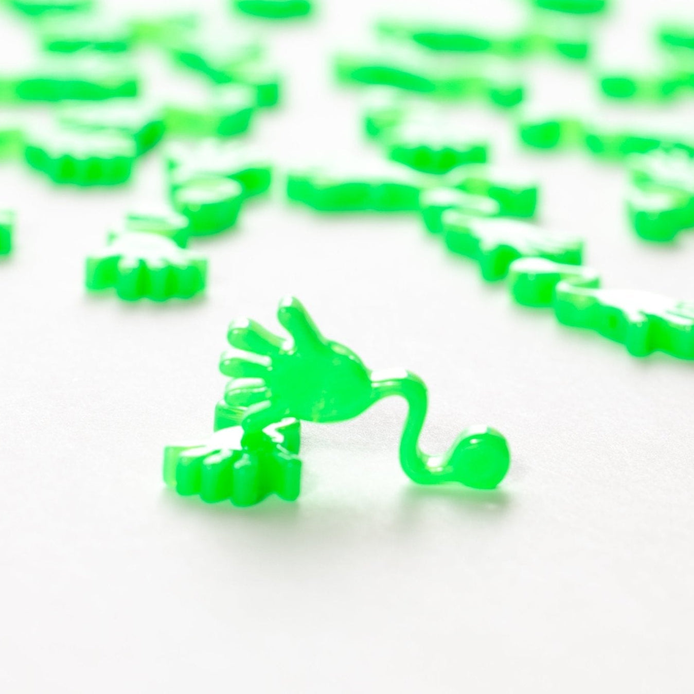 Close-up of one green sticky hand kandi bead with a wavy arm, more blurred behind