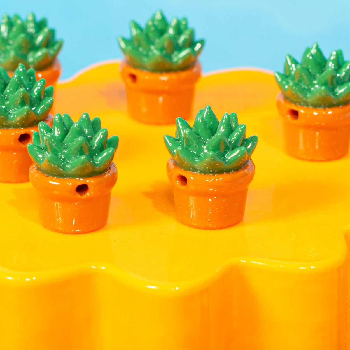 Close-up of green succulent kandi beads in glittery orange pots on a yellow riser