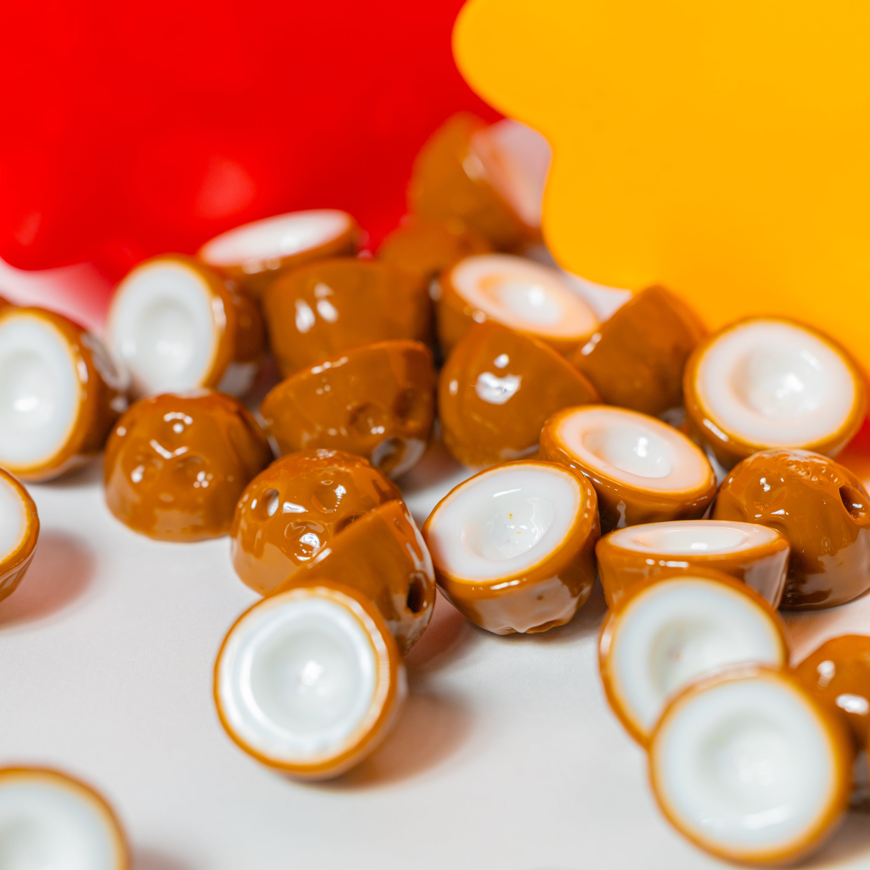 Coconut kandi beads scattered on white, brown three-pore husks and white flesh halves, warm backdrop