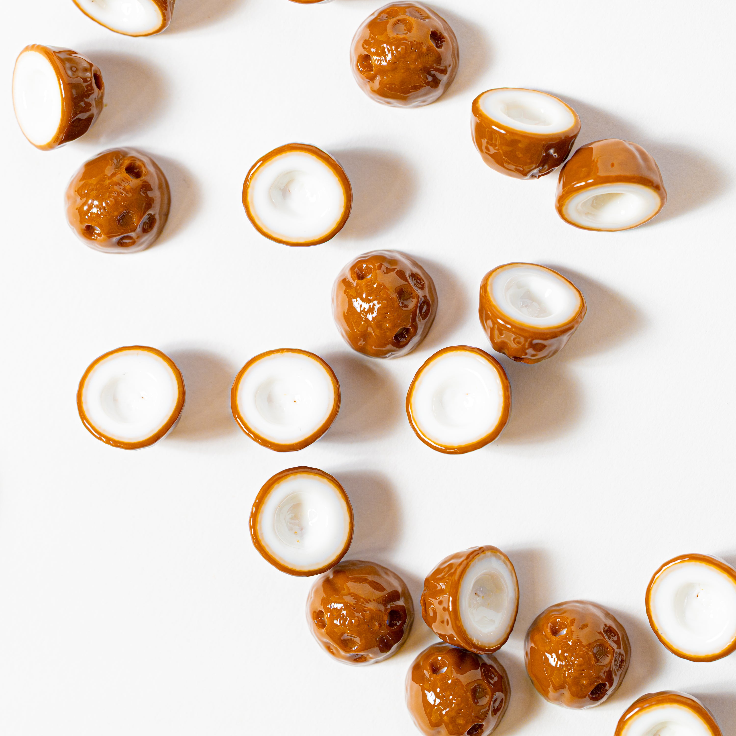 Coconut kandi beads scattered on white from above, some showing white flesh, others the brown husk with three pores