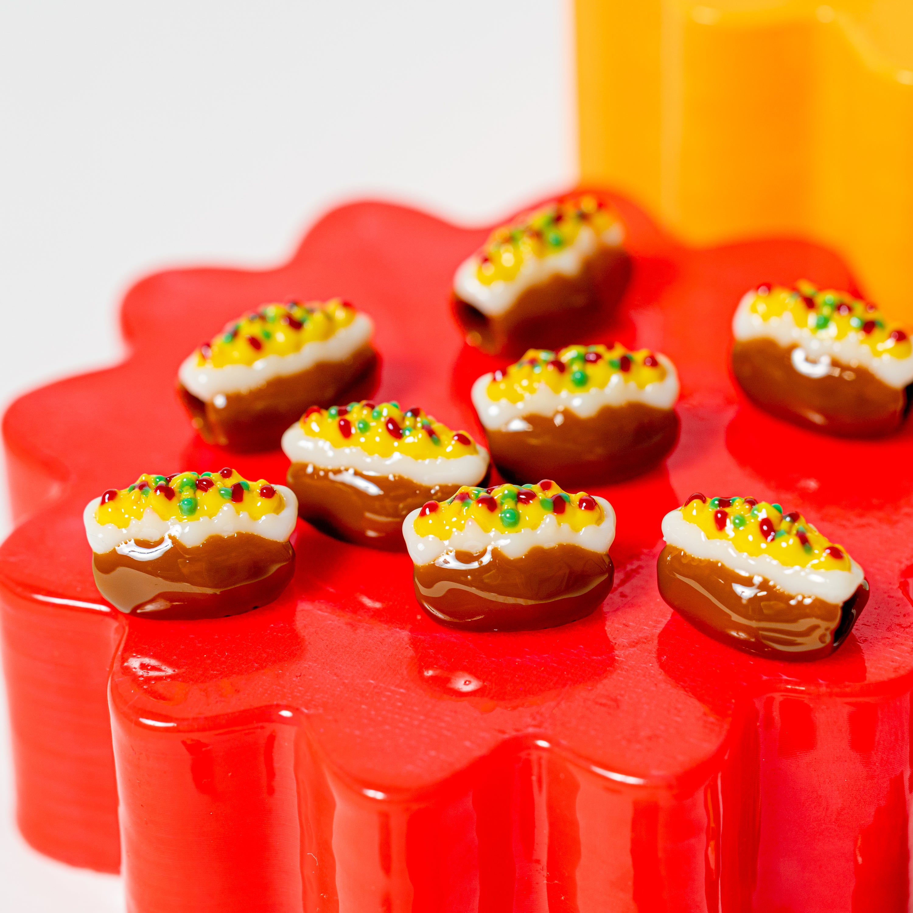 Baked potato kandi beads with cheese and bacon bits clustered on a red flower riser, orange block behind