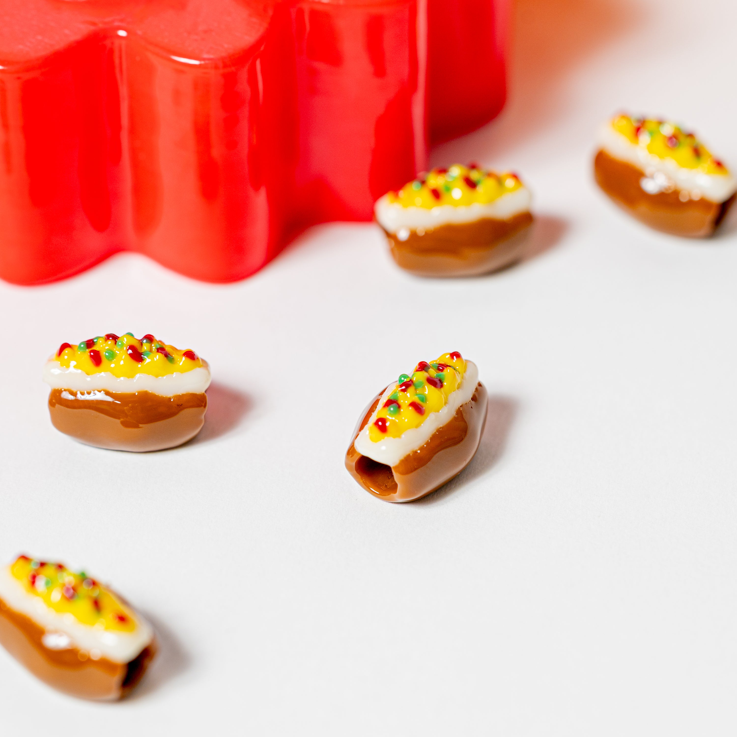 Close-up of baked potato kandi beads on white, one tipped to show its drilled hole, red riser behind