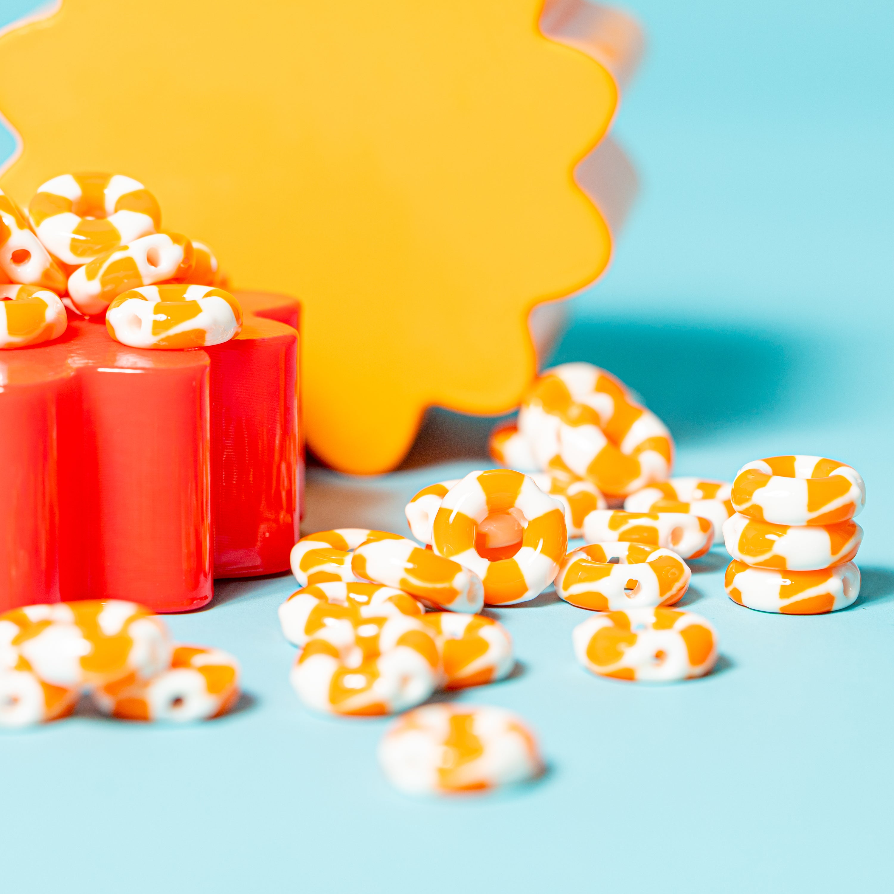 Orange and white life preserver kandi beads spilling from a red riser onto teal, yellow shape behind