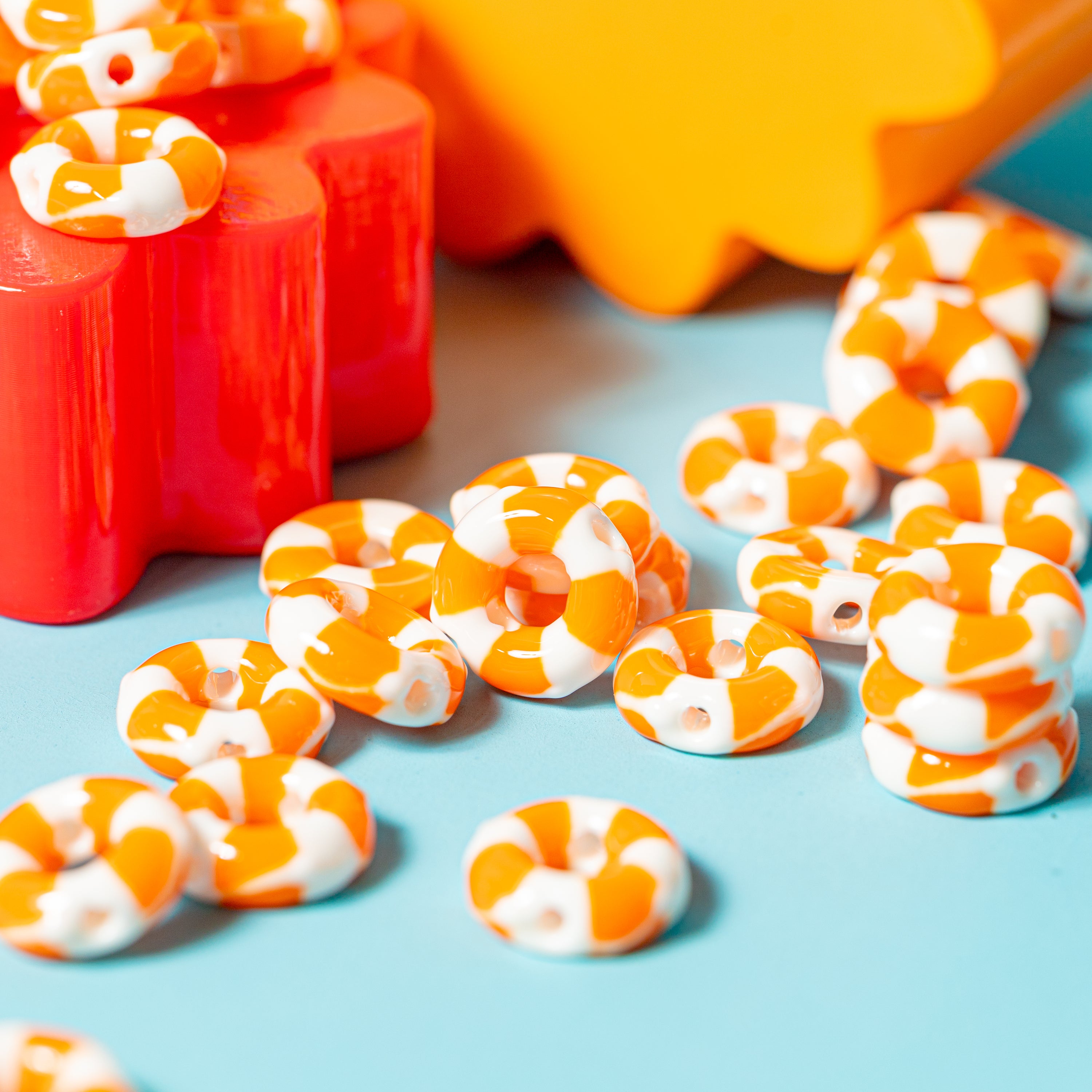Close-up of orange and white life preserver kandi beads scattered on teal, drilled holes visible, red and yellow behind