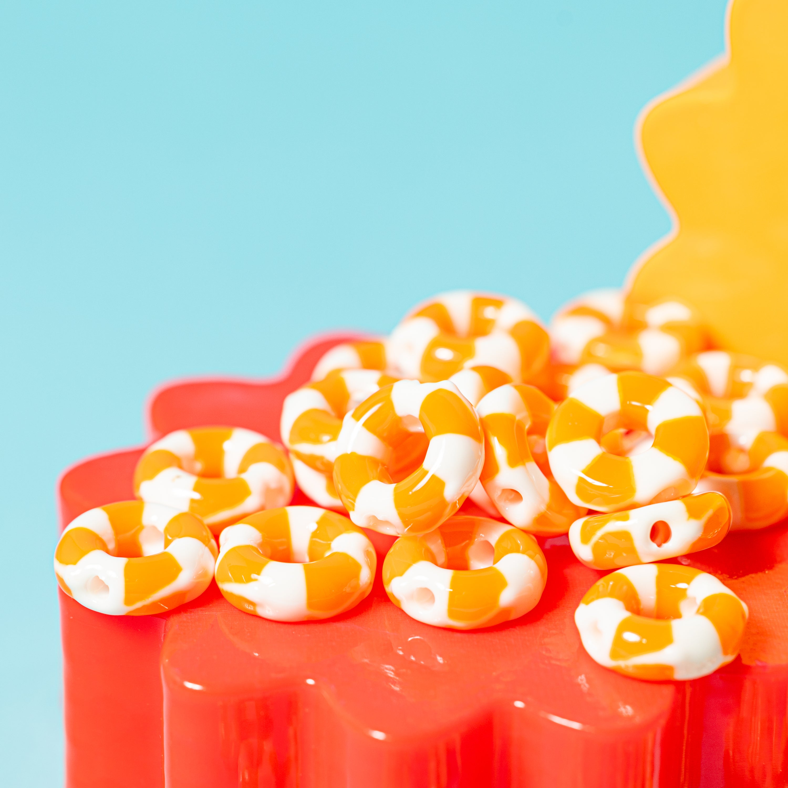 Orange and white life preserver kandi beads piled on a red flower riser, yellow and teal behind