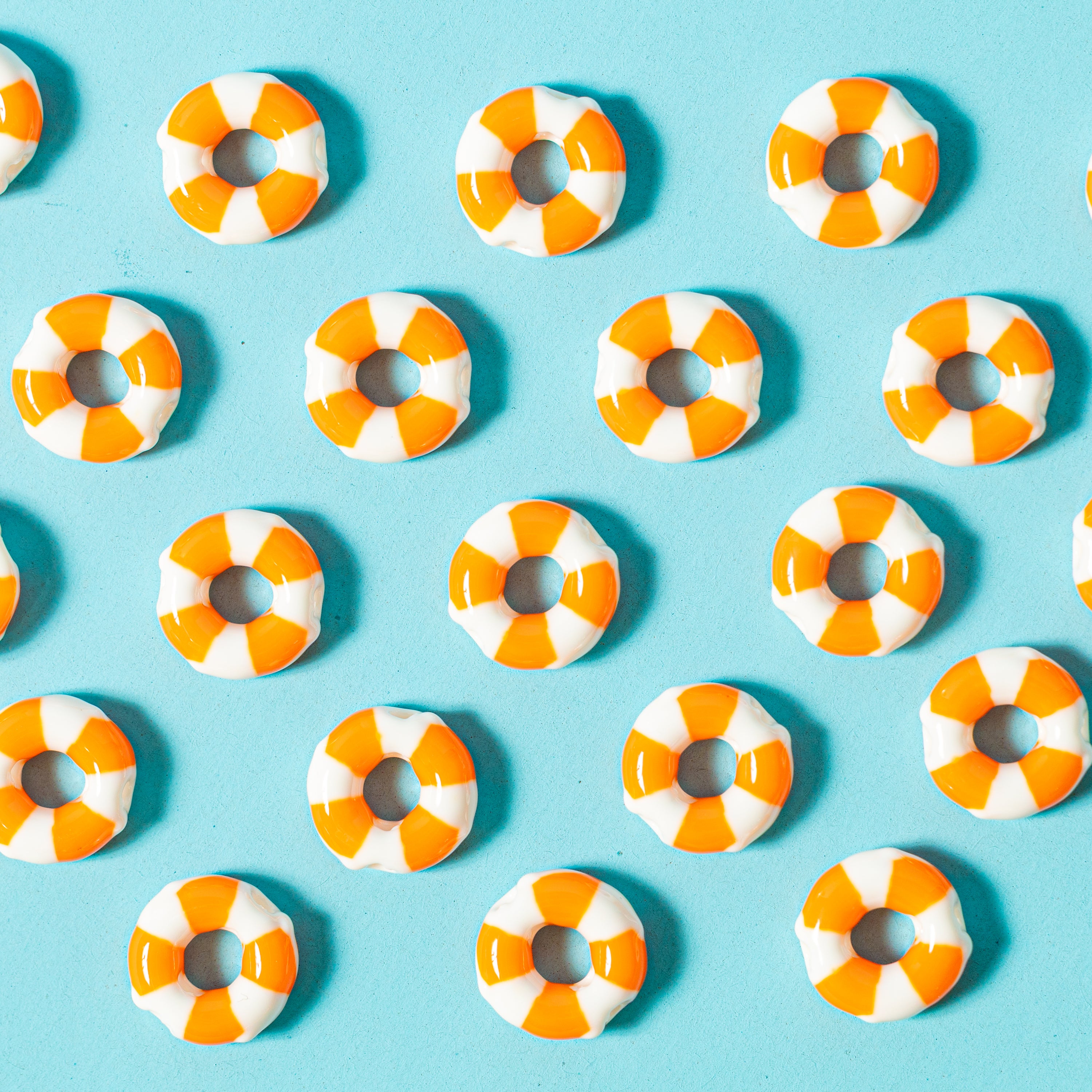 Orange and white life preserver ring kandi beads laid out in an even grid on teal, from above