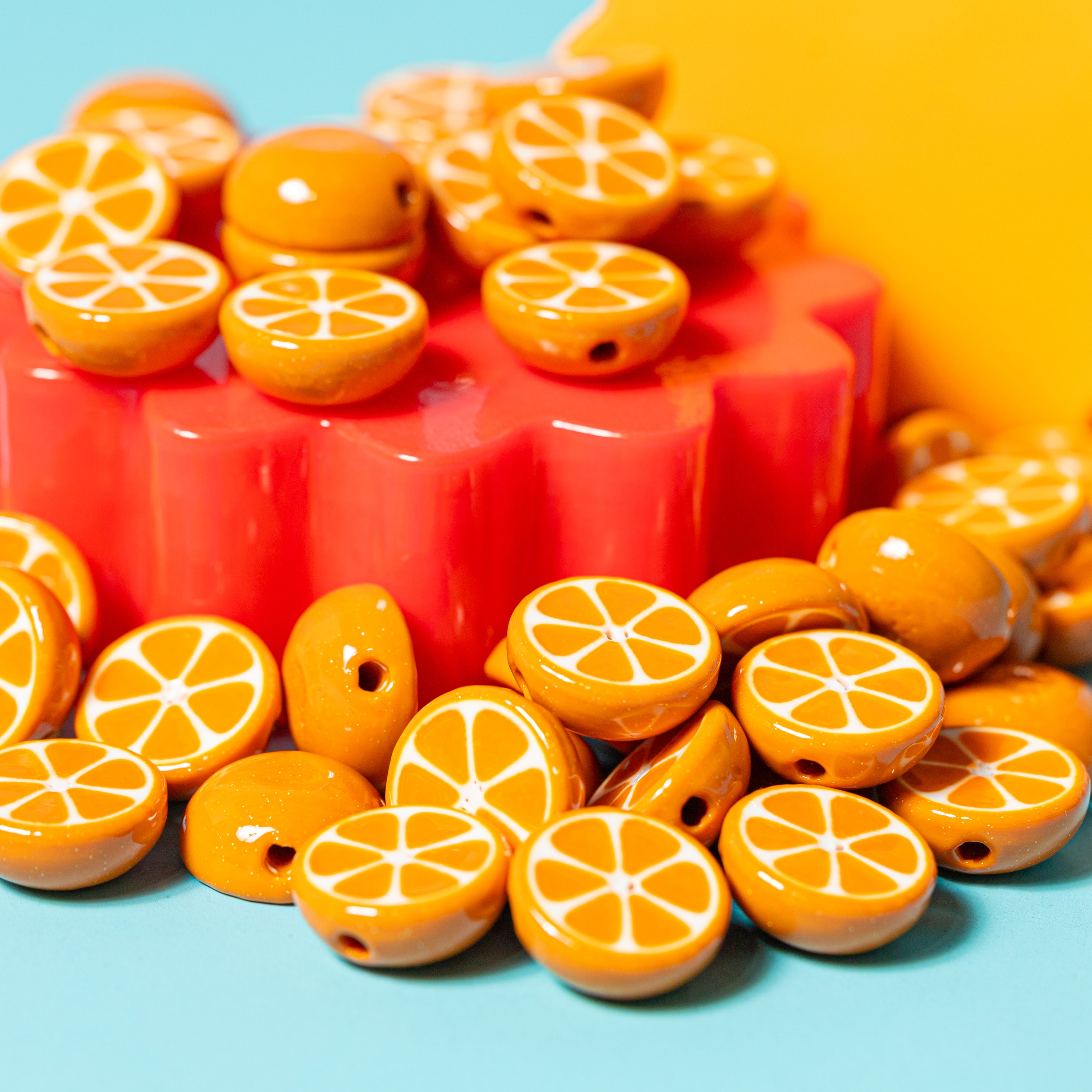 Orange slice beads for kandi bracelets piled on a red flower riser, yellow and teal behind