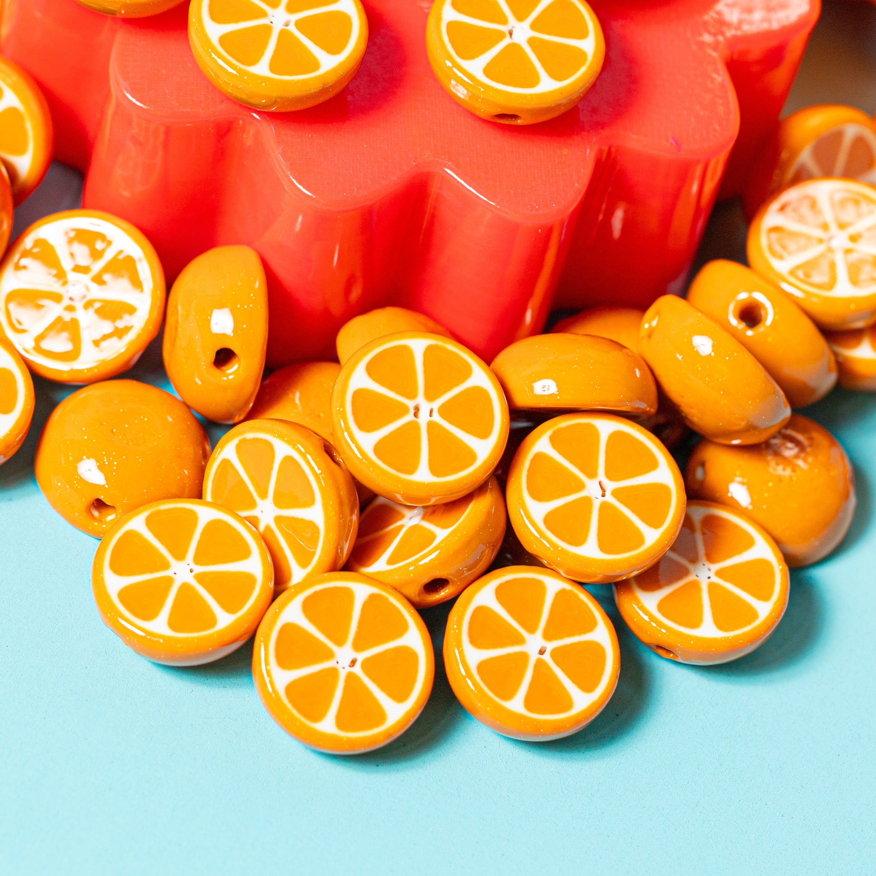 Orange citrus kandi beads spilling from a red riser onto teal, some showing slice segments, others whole-orange backs