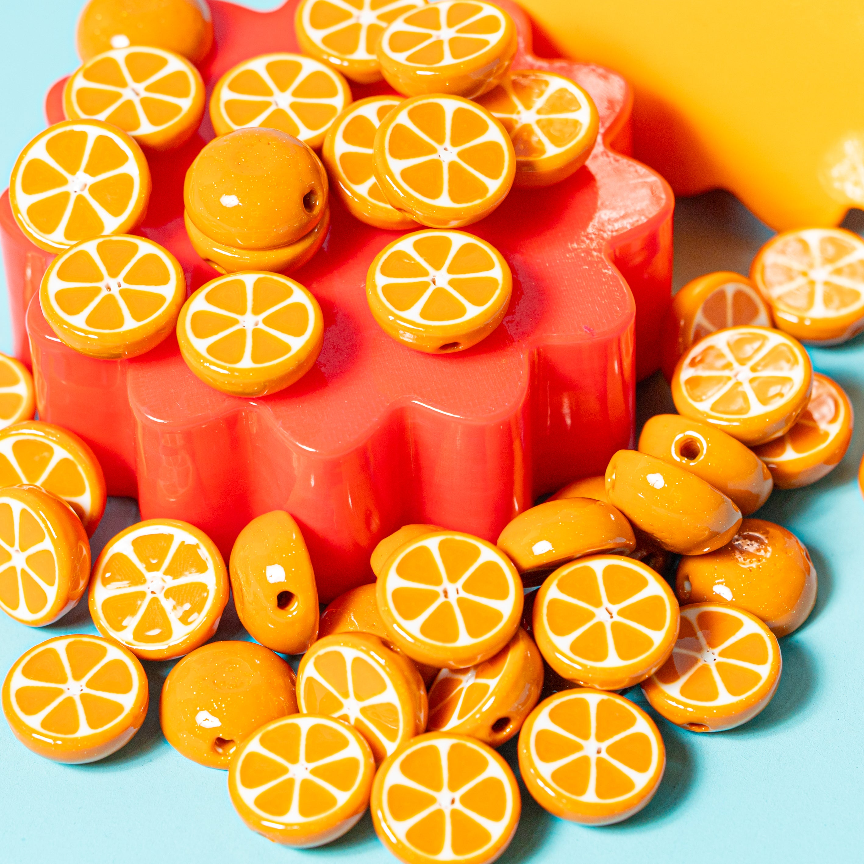 Orange citrus kandi beads heaped on a red flower riser with more scattered on teal, yellow behind