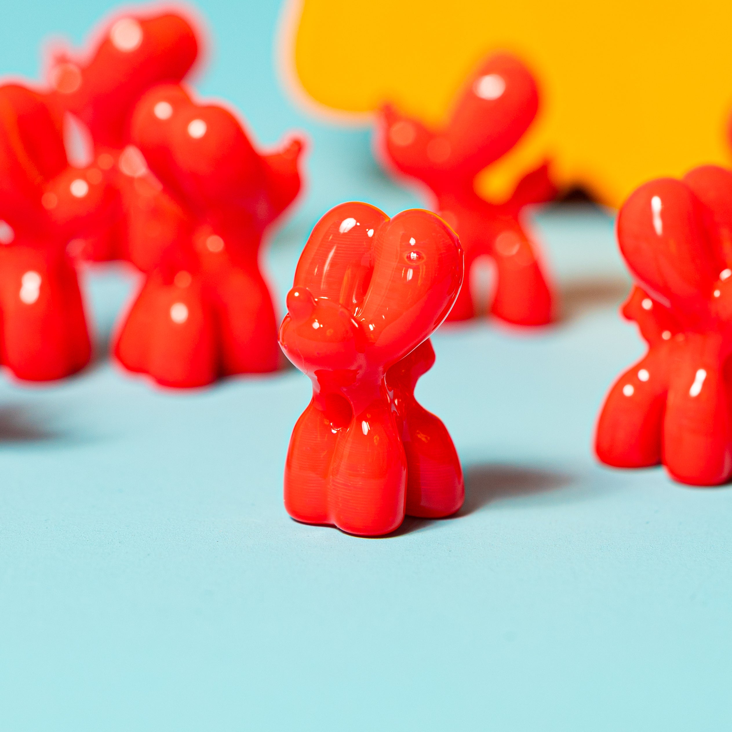 A red balloon dog kandi bead in sharp focus among a crowd of blurred red balloon dogs, teal and yellow behind