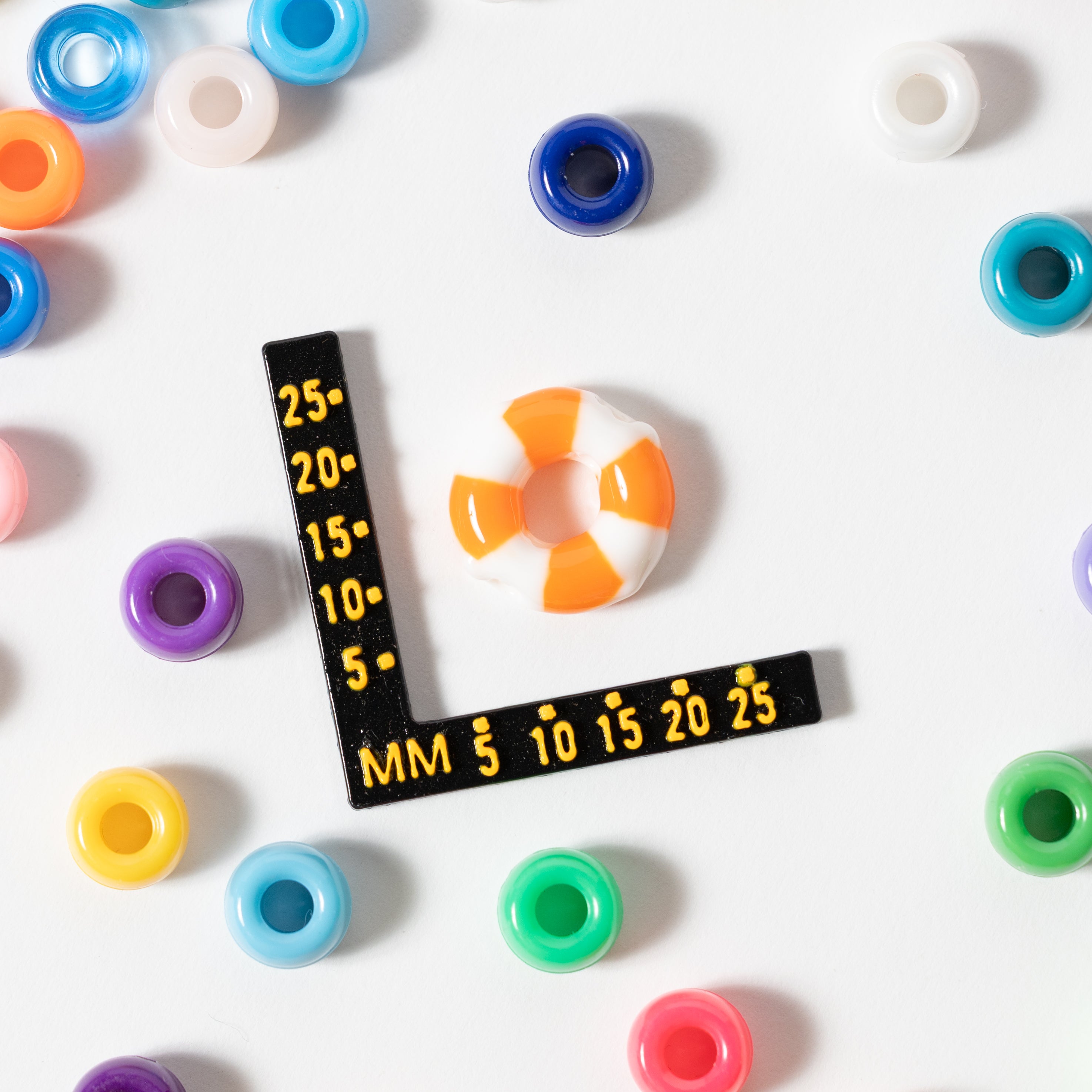 Size guide: an orange and white life preserver kandi bead beside a millimeter ruler, rainbow pony beads around