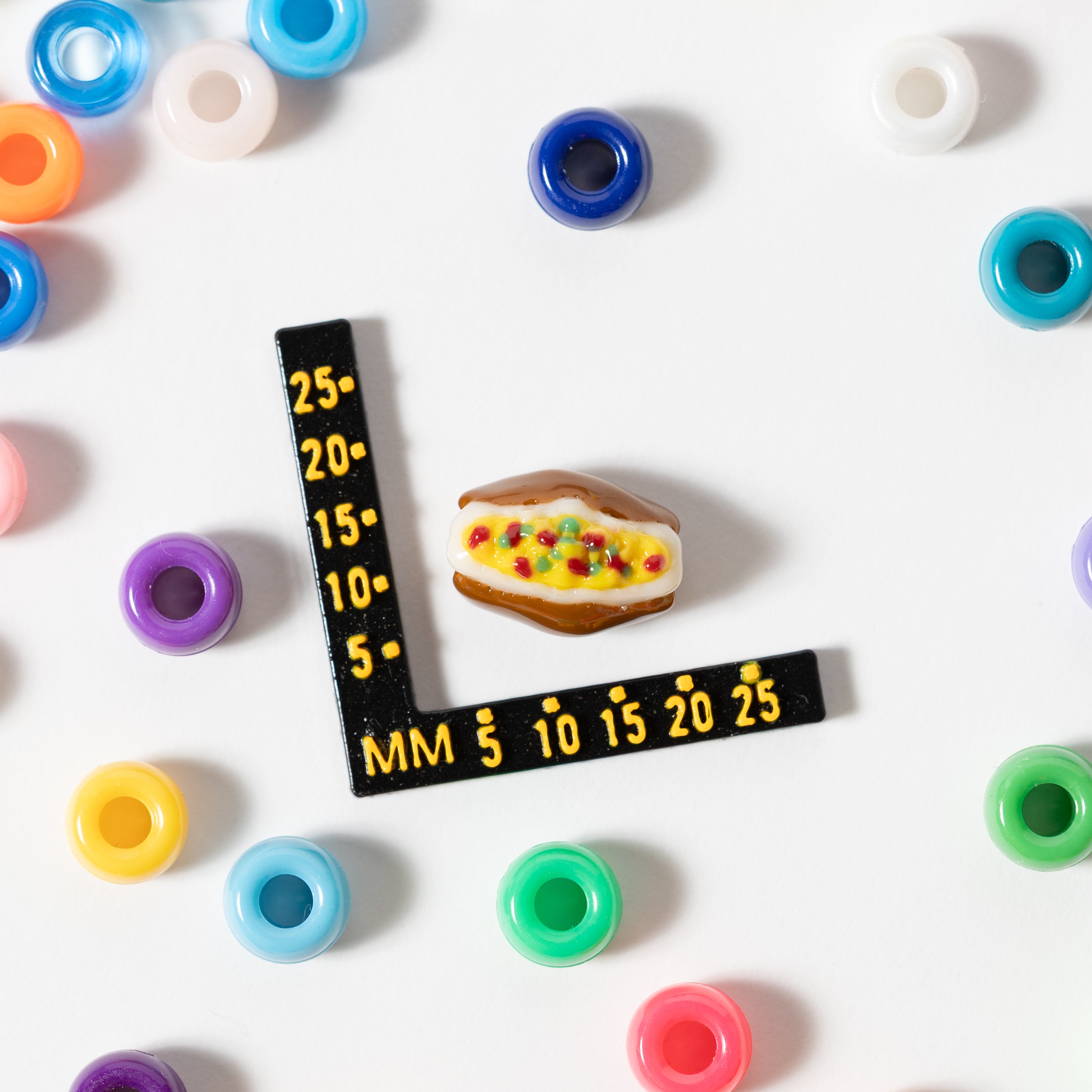 Size guide: a loaded baked potato kandi bead beside a millimeter ruler, surrounded by rainbow pony beads