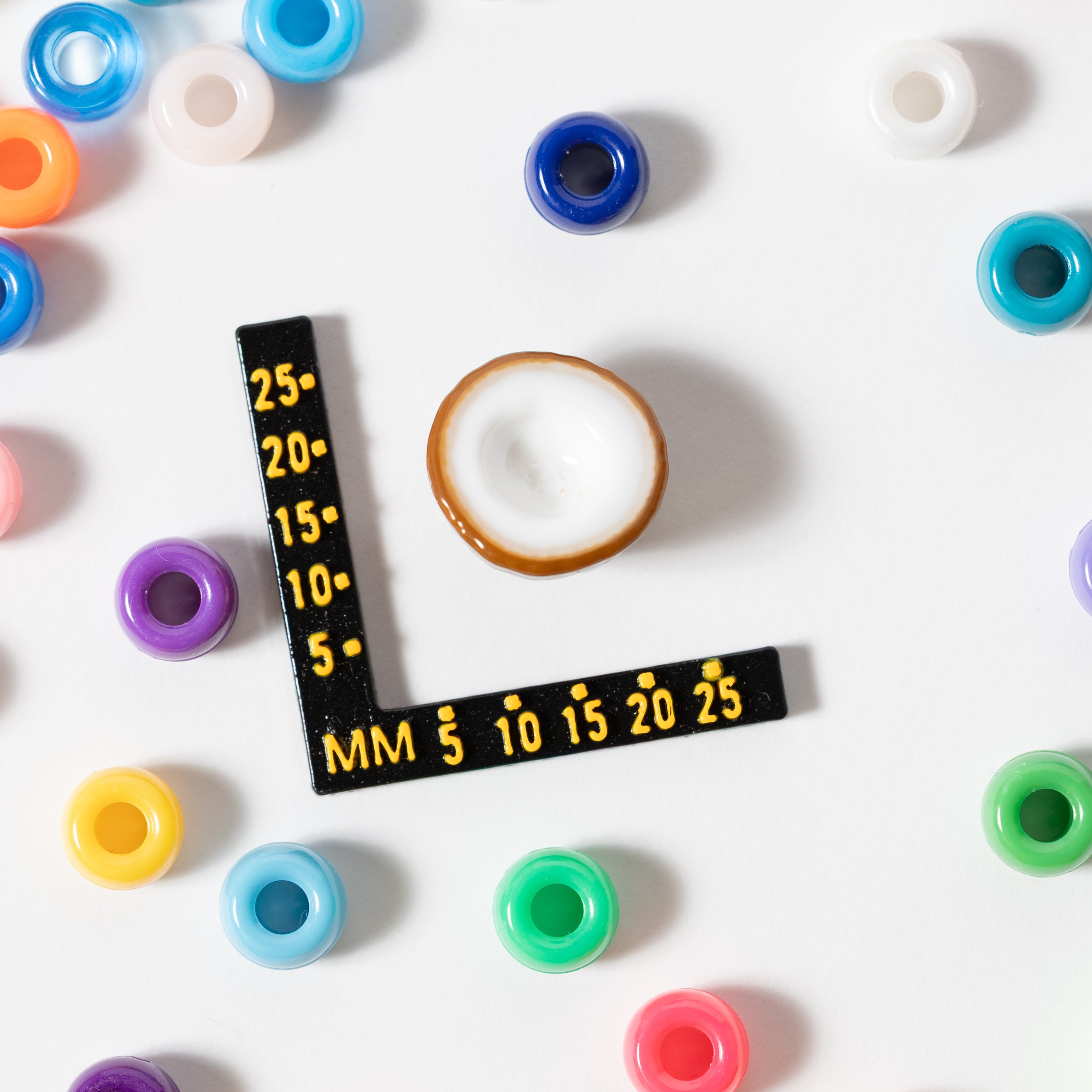 Size guide: a coconut kandi bead beside a millimeter ruler, surrounded by rainbow pony beads