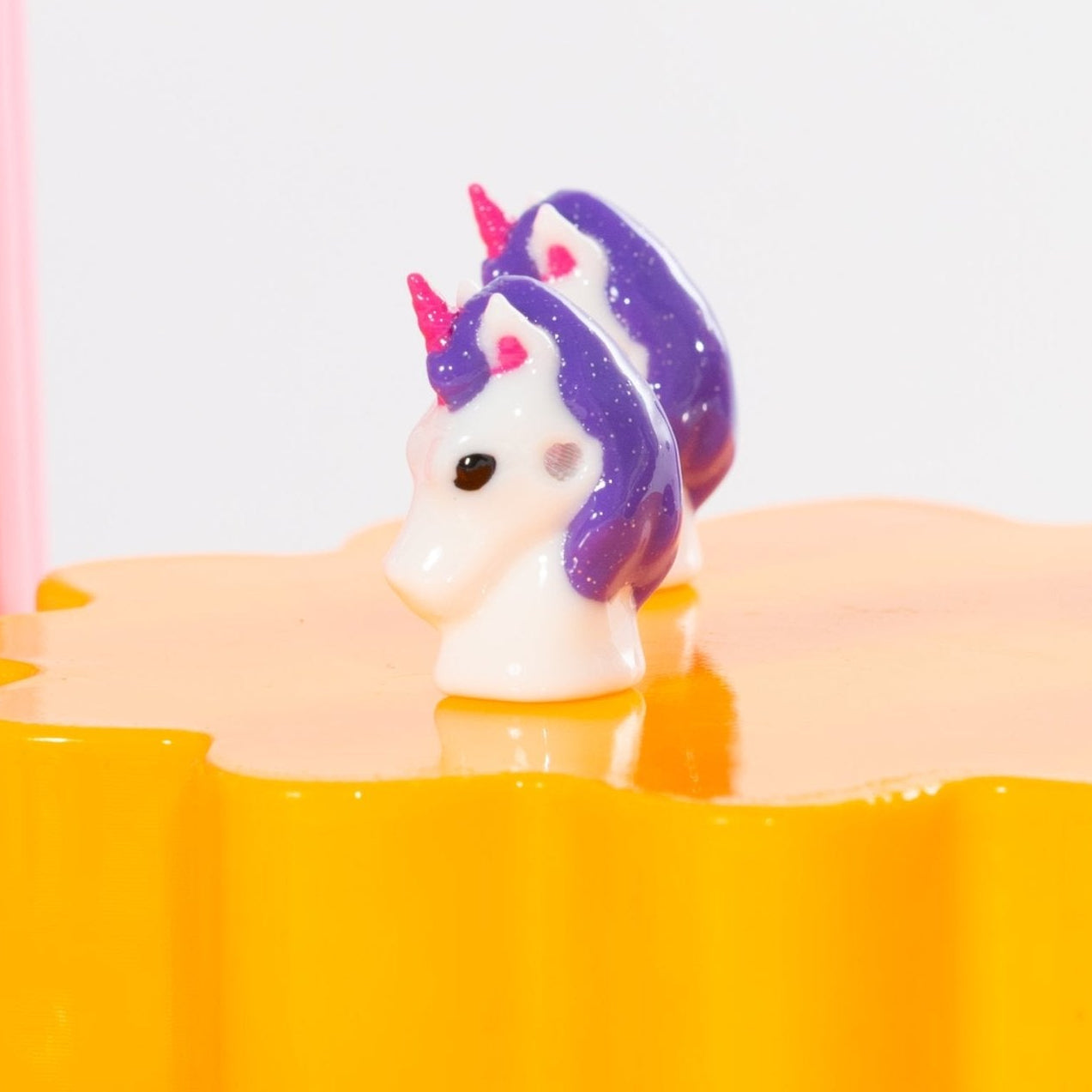 A purple-maned unicorn kandi bead on an orange riser, pink block at the edge