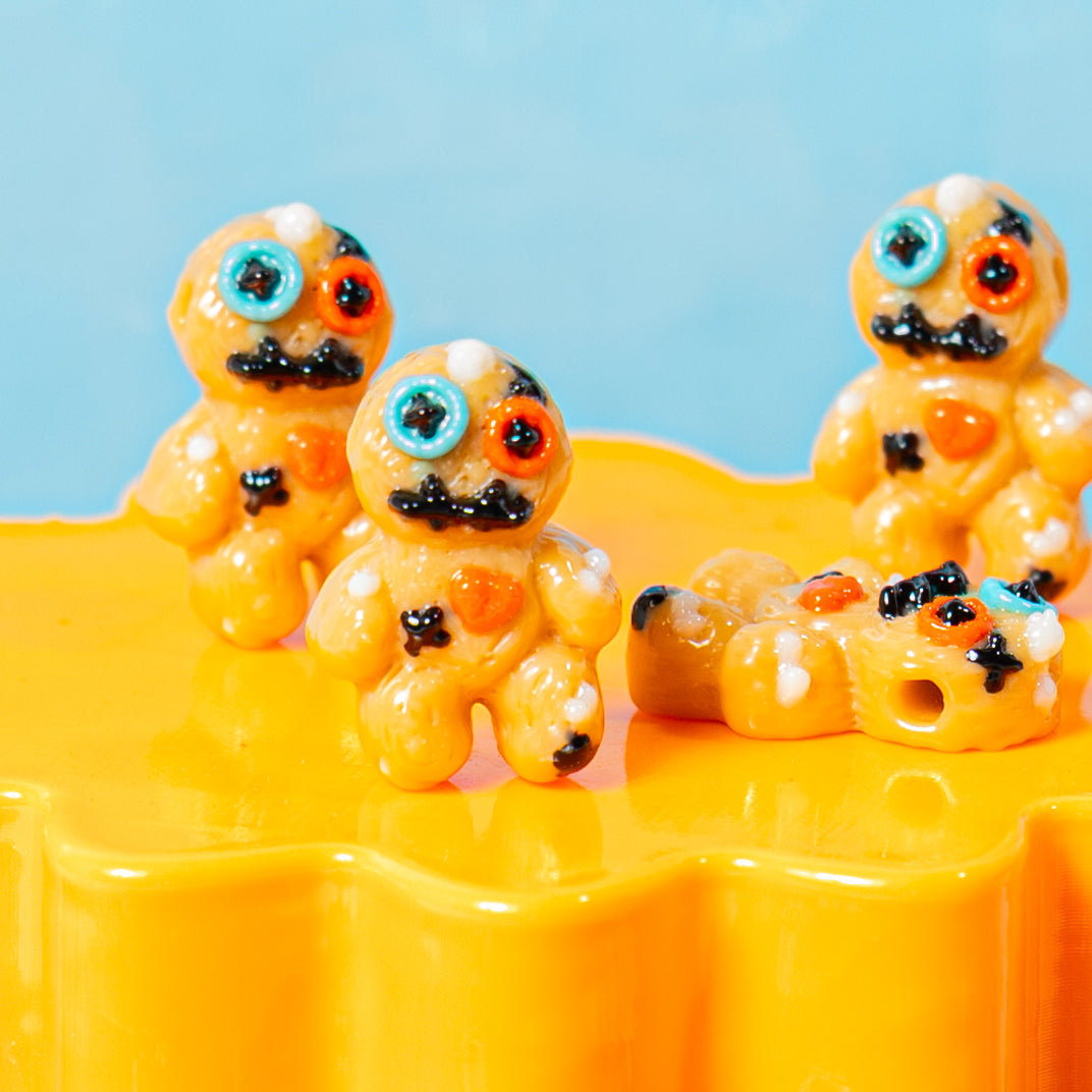 Close-up of tan voodoo doll kandi beads with button eyes and stitched mouths on an orange riser