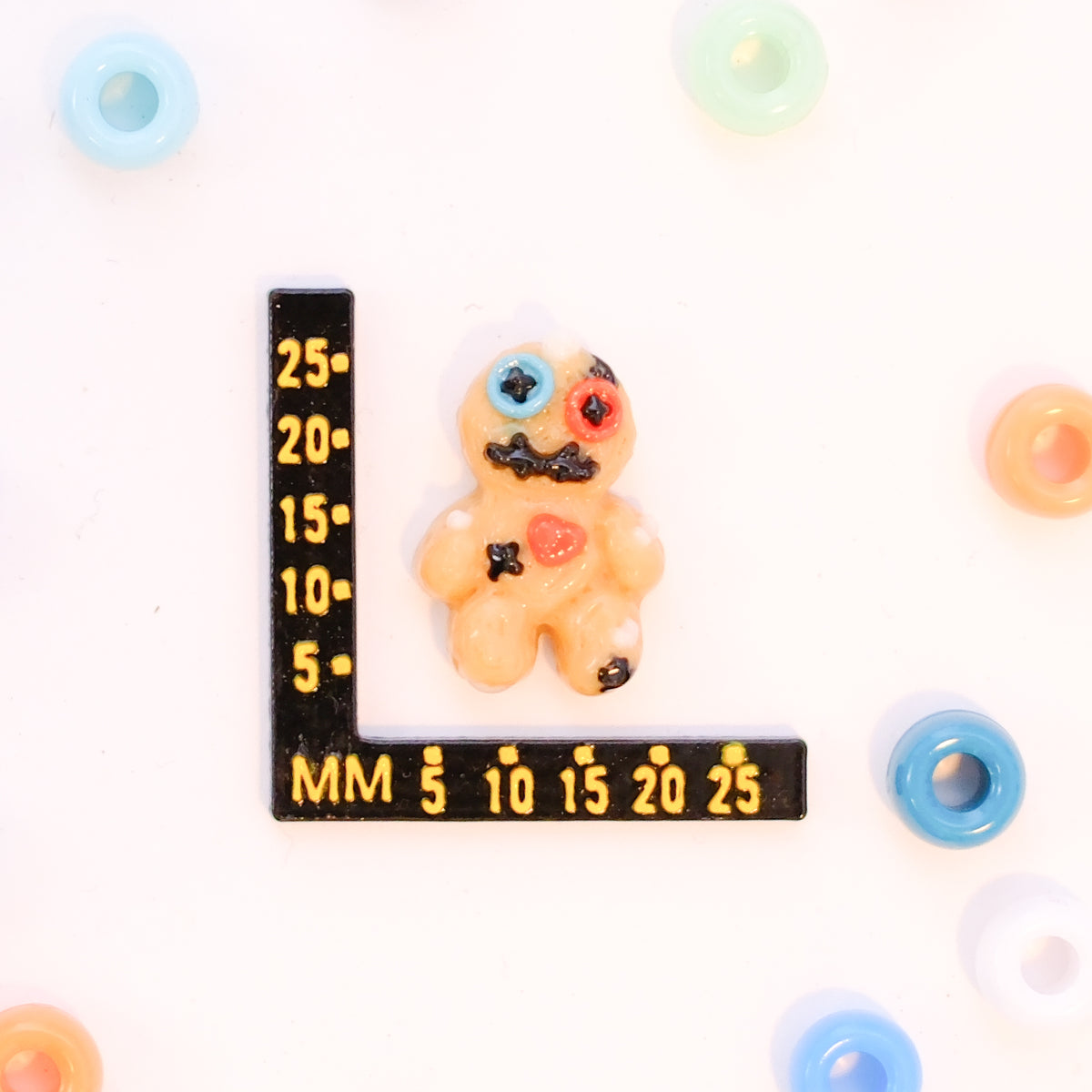 Size guide: a voodoo doll kandi bead beside a millimeter ruler for scale