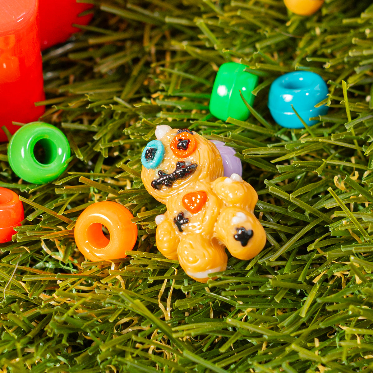 Voodoo doll kandi bead sitting in green grass beside colorful beads